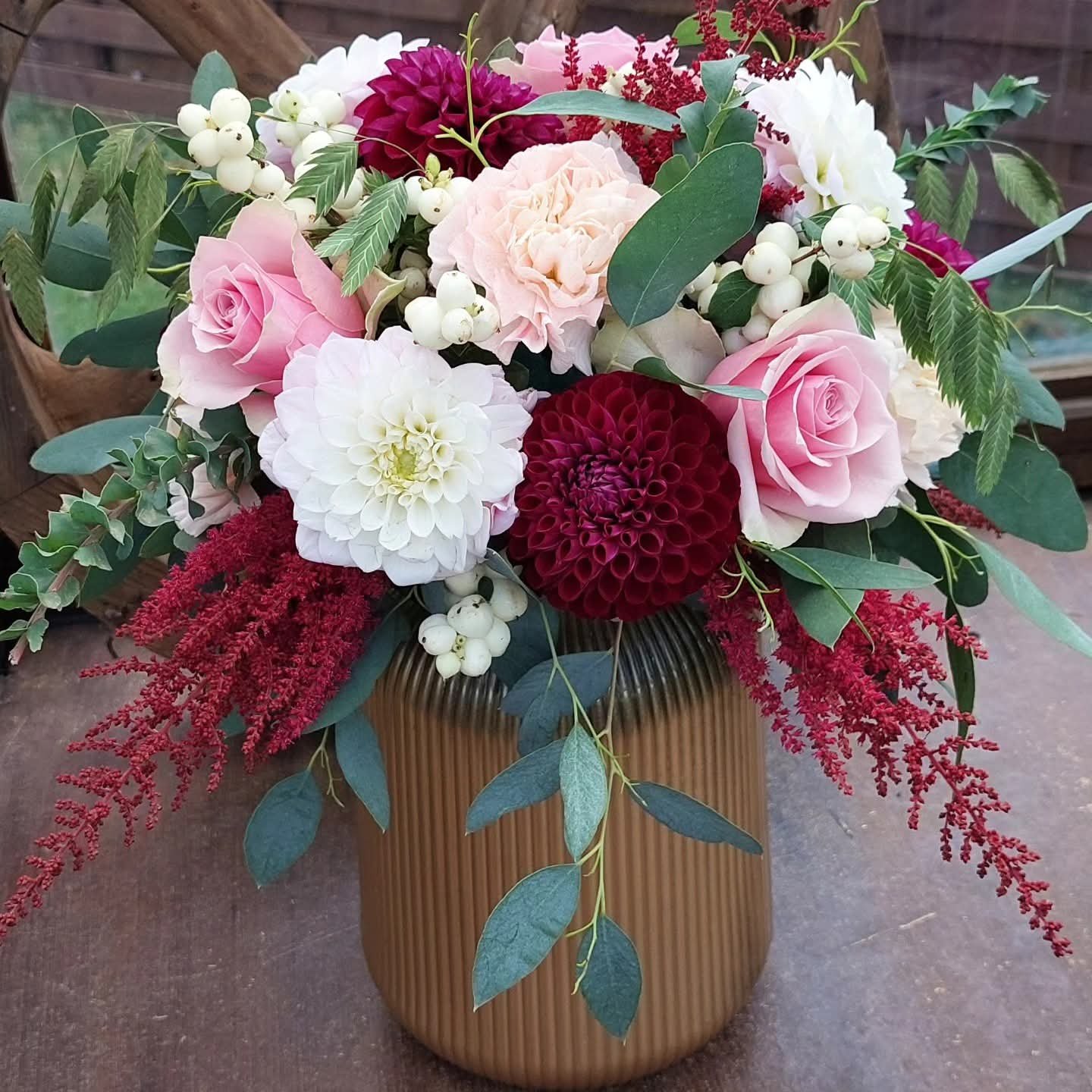 Bouquet de fleurs dans un vase marron avec roses roses, dahlias blancs et rouges, feuilles vertes et baies blanches.
