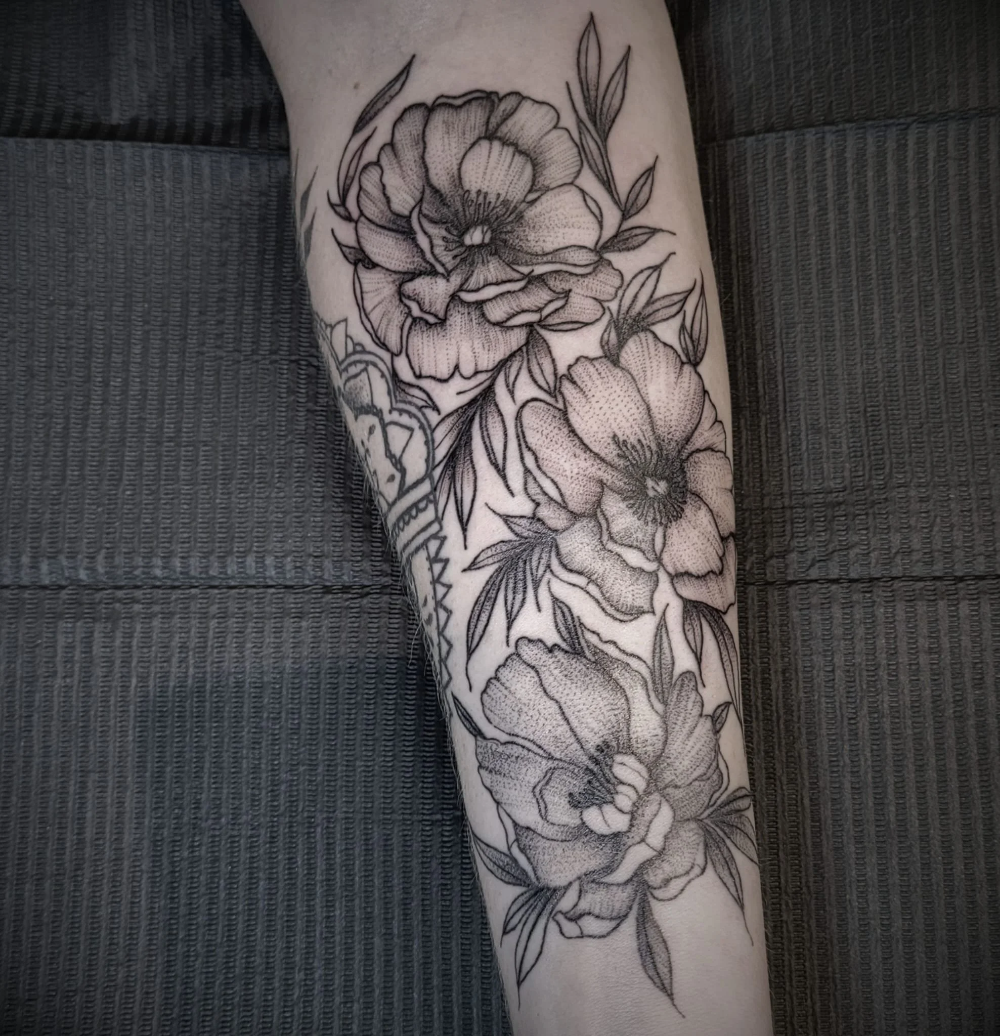 Black and grey floral tattoo on person's arm, featuring large flowers with detailed petals and leaves.
