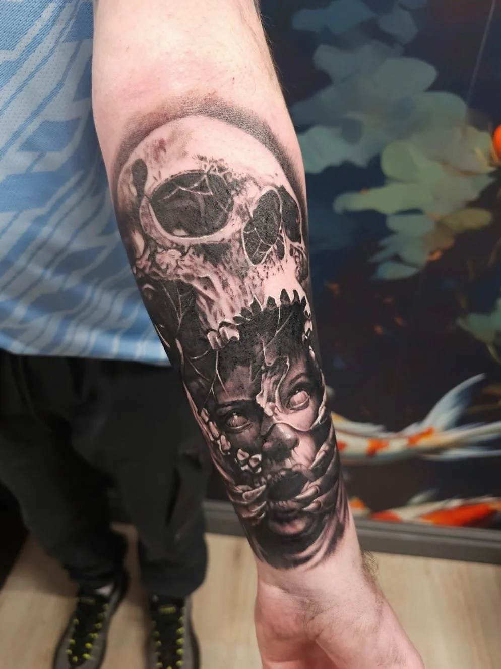 Black and gray tattoo of a skull above an illustration of a child's face on a person's forearm.