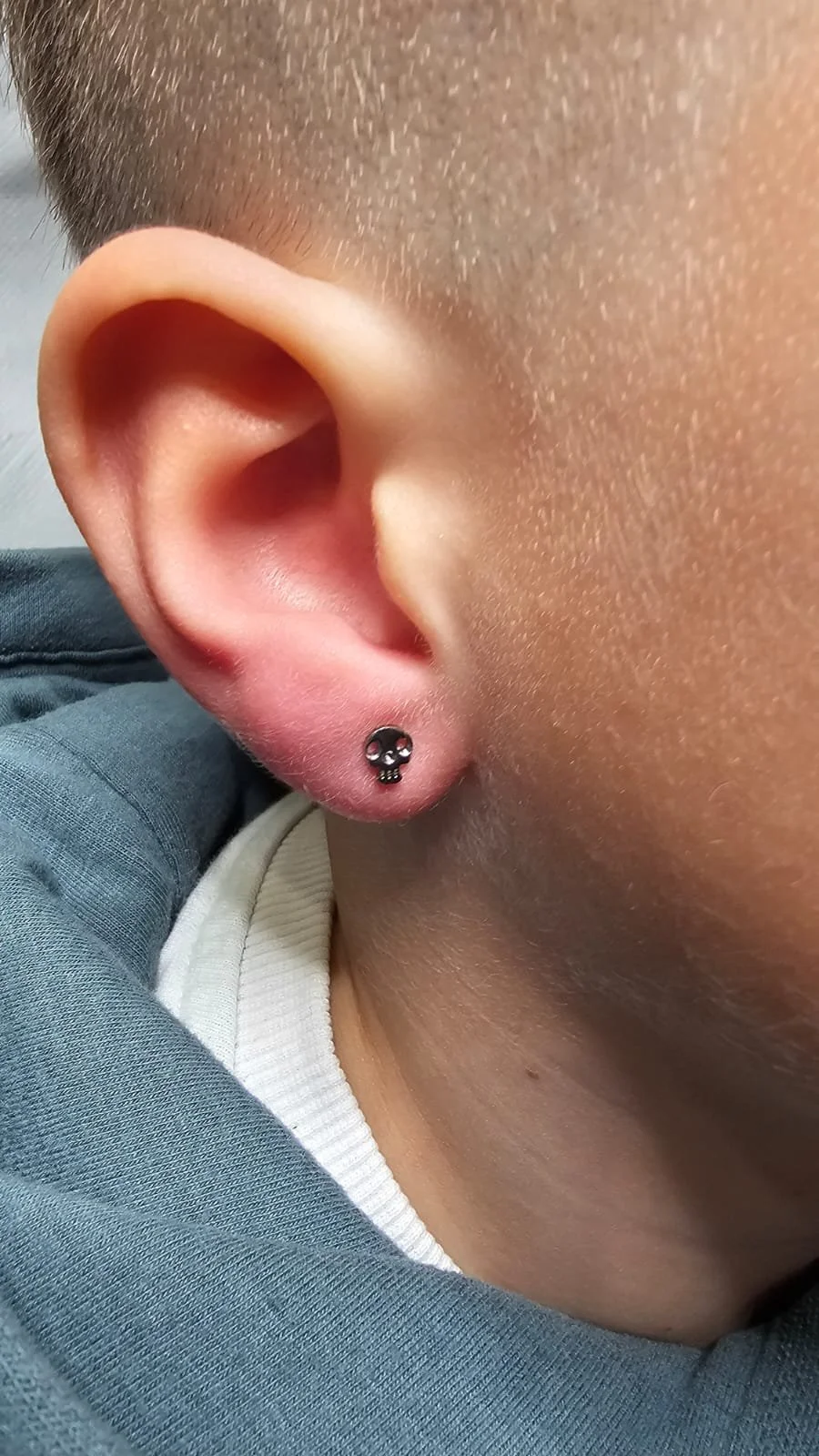 Close-up of a person's ear with a small skull-shaped stud earring.