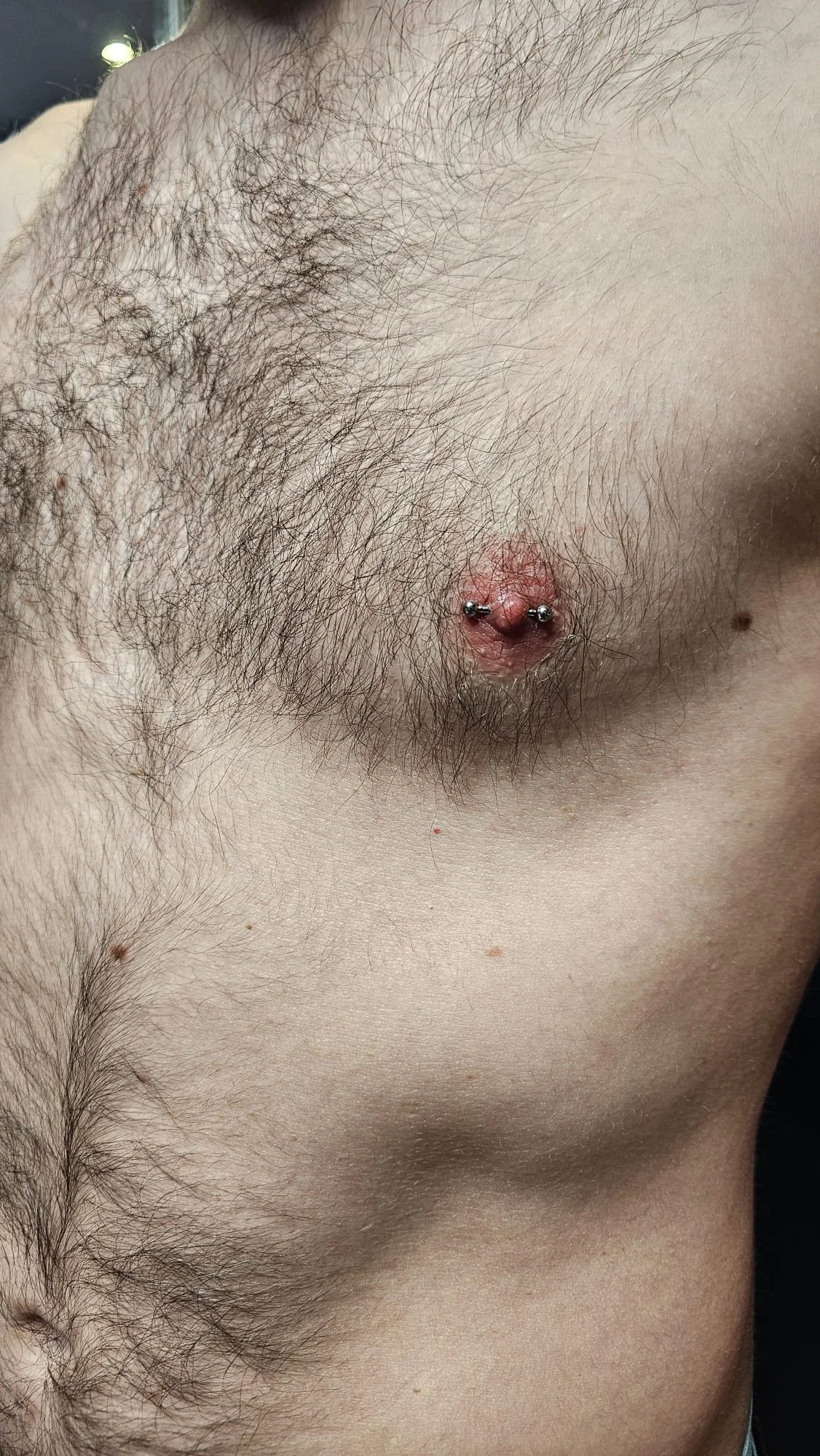 Close-up of a male's chest with an asymmetrical piercings on the left nipple.