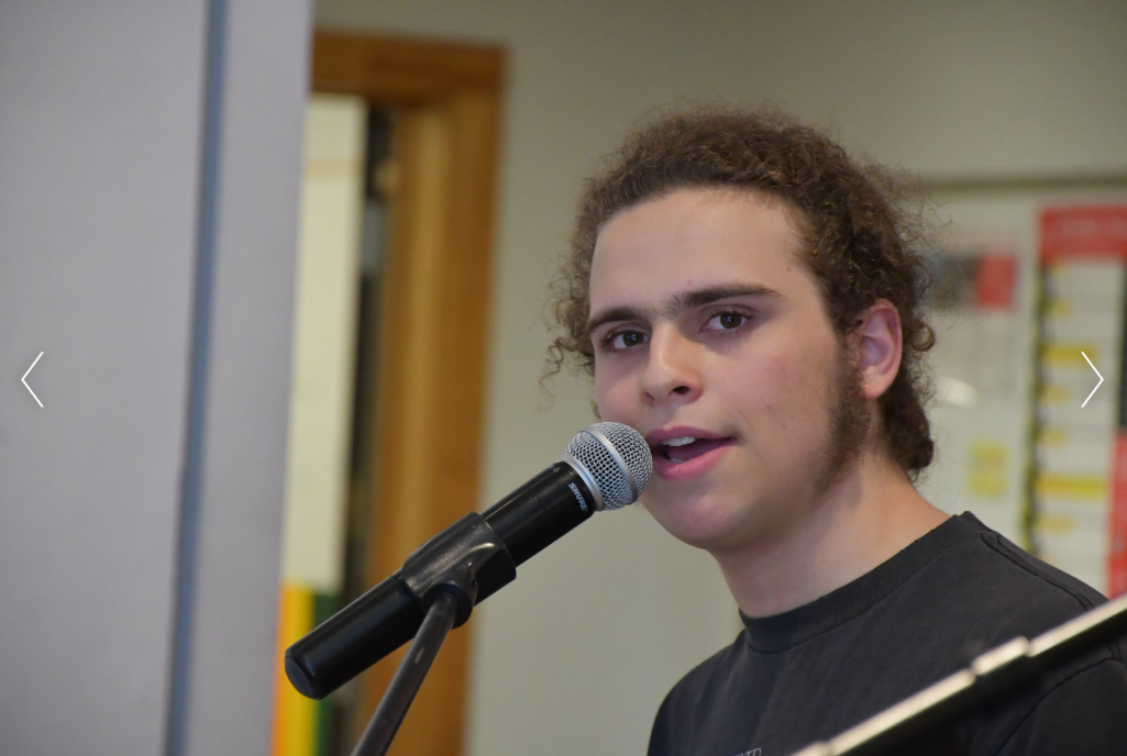 A young person with curly hair speaking into a microphone.
