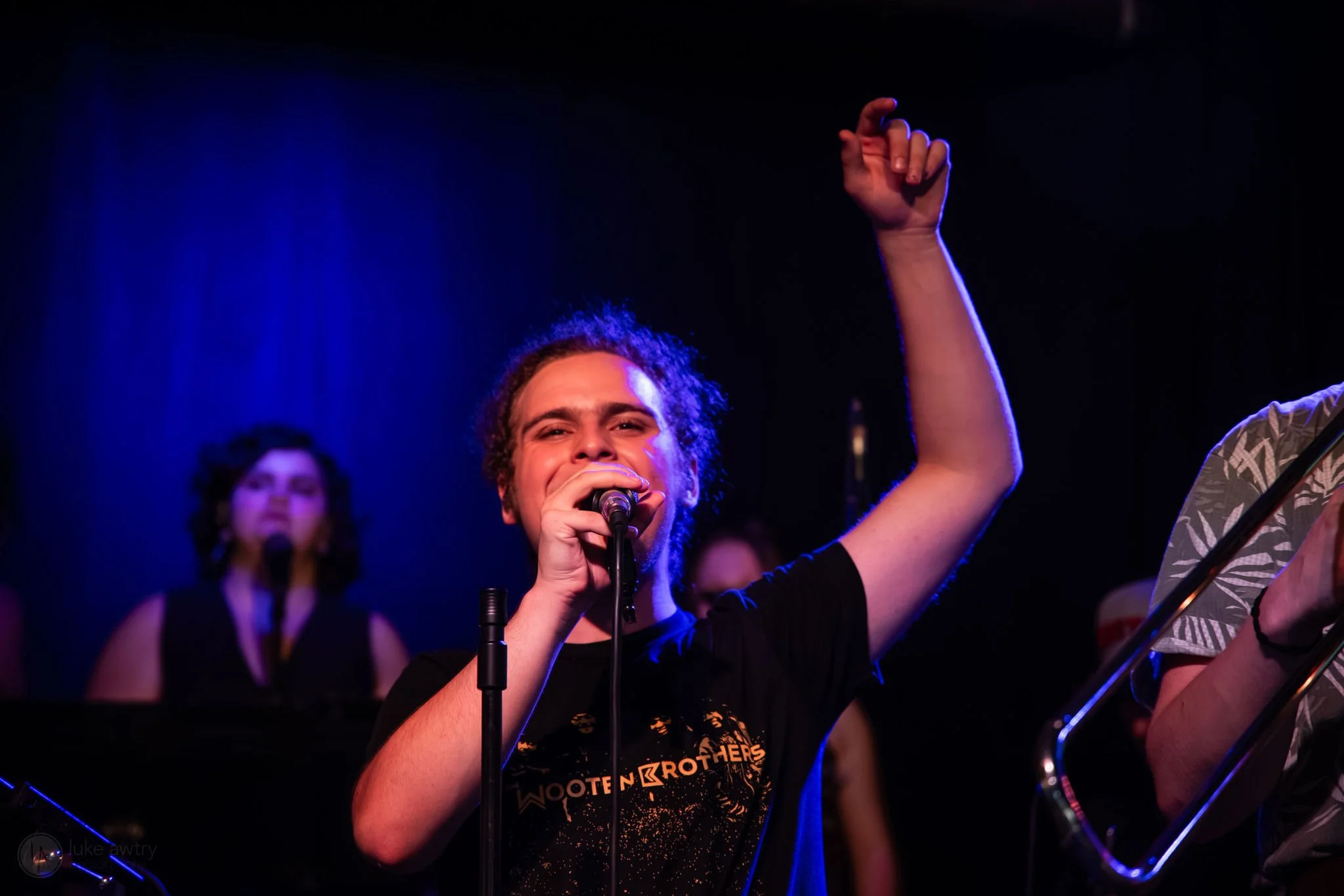 Young person with curly hair holding a MIDI controller keyboard in front of a red curtain.