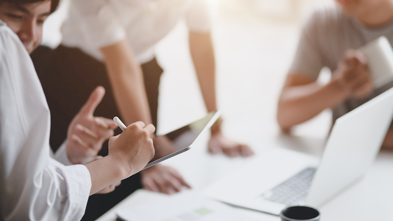 office workers collaborating around a white table using laptops and tablet devices