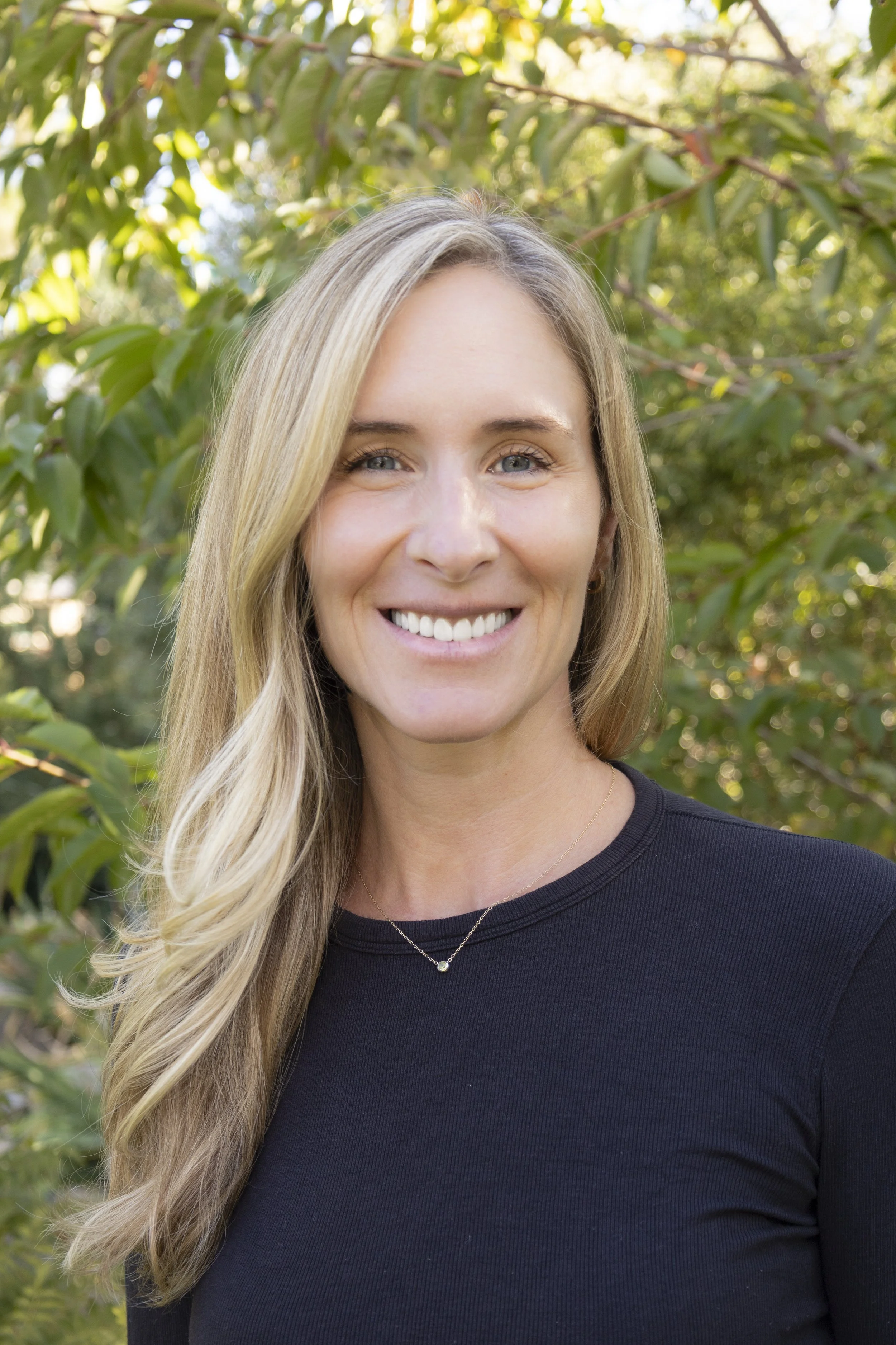 photo of jessica abrass wearing a black crew-neck shirt in front of leafy green trees