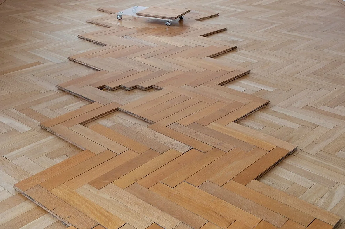 Wooden floor in the process of being refinished, with some planks removed and a skateboard in the background.
