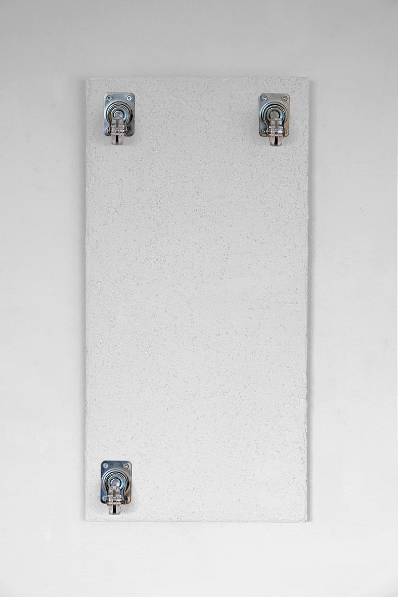 An empty white electrical panel with three metal latches on a wall.