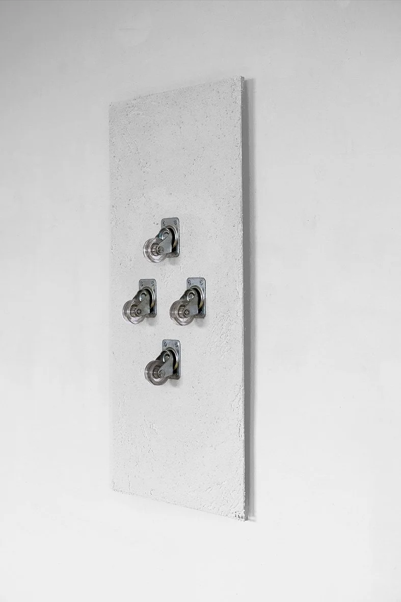 A white textured wall with four small caster wheels mounted on it.