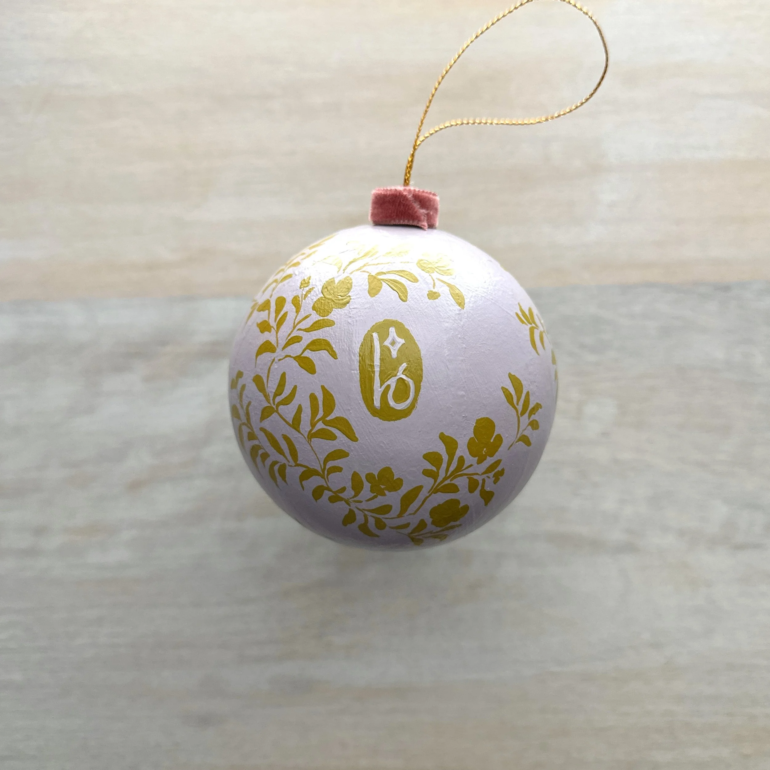 Hand painted paper mache holiday ornament with purple and olive green botanicals showing Blair Frazier Art logo on back.