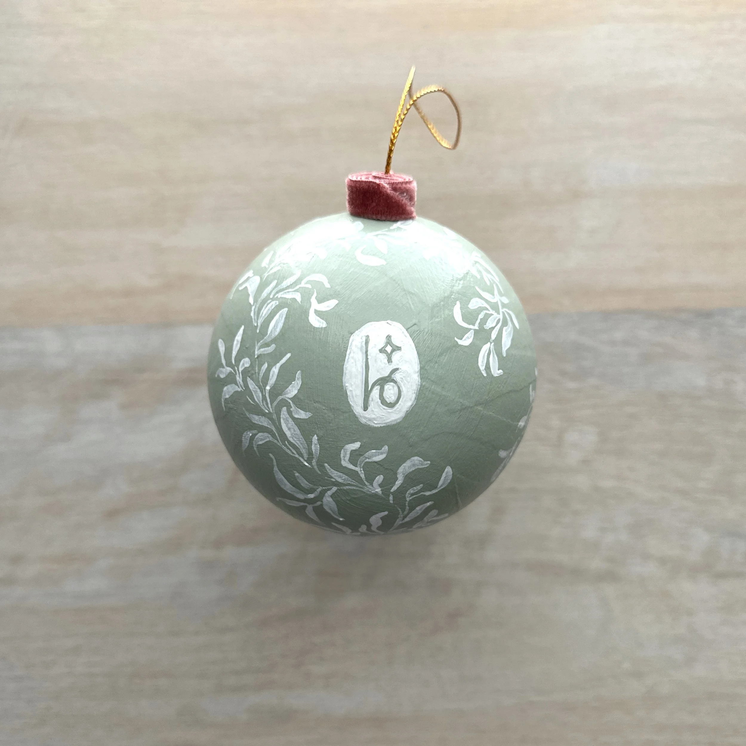 Light blue-green Christmas ornament with white botanical design and dusty rose velvet cap with Blair Frazier Art logo