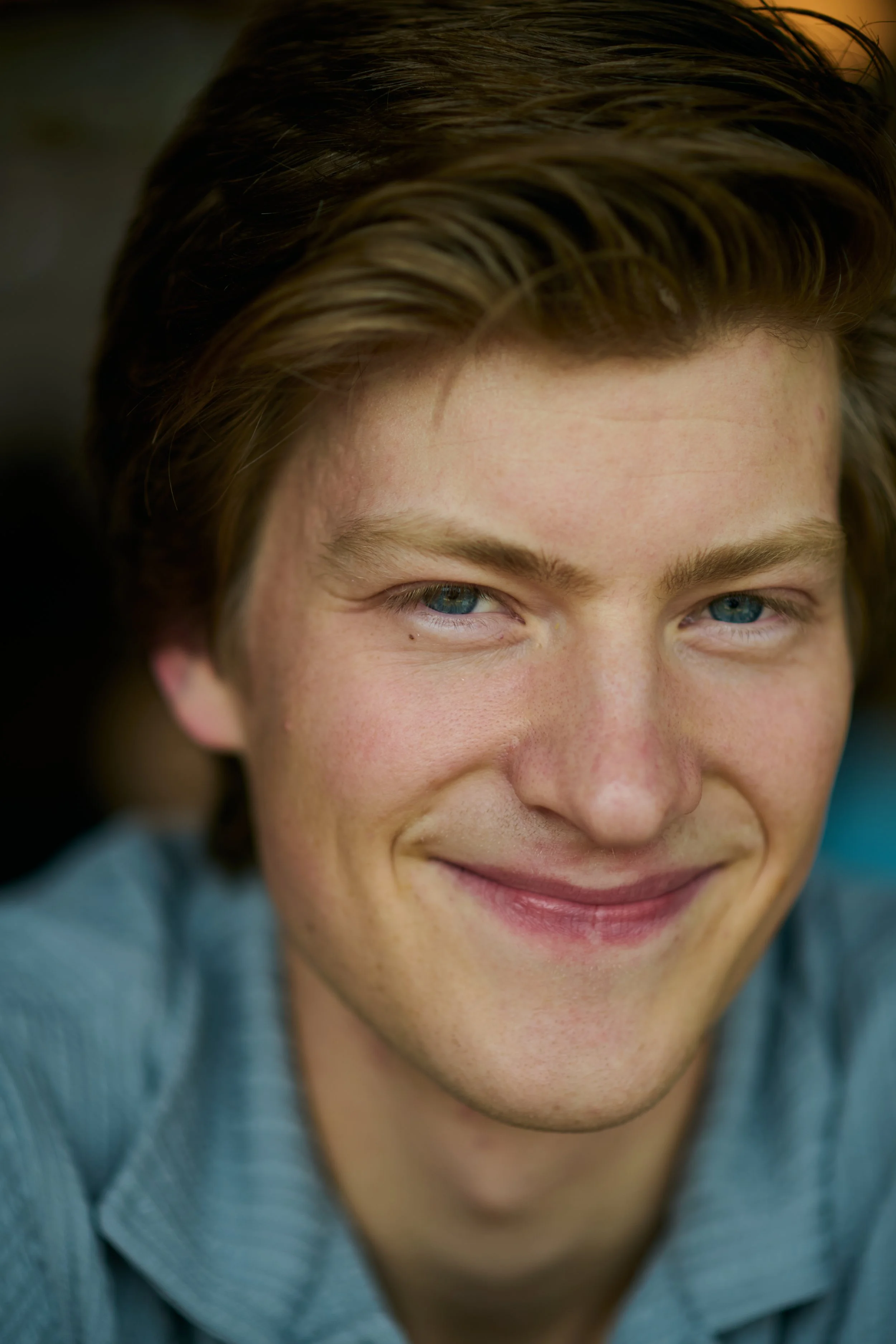 Close-up of a young man with brown hair and blue eyes, smiling at the camera.