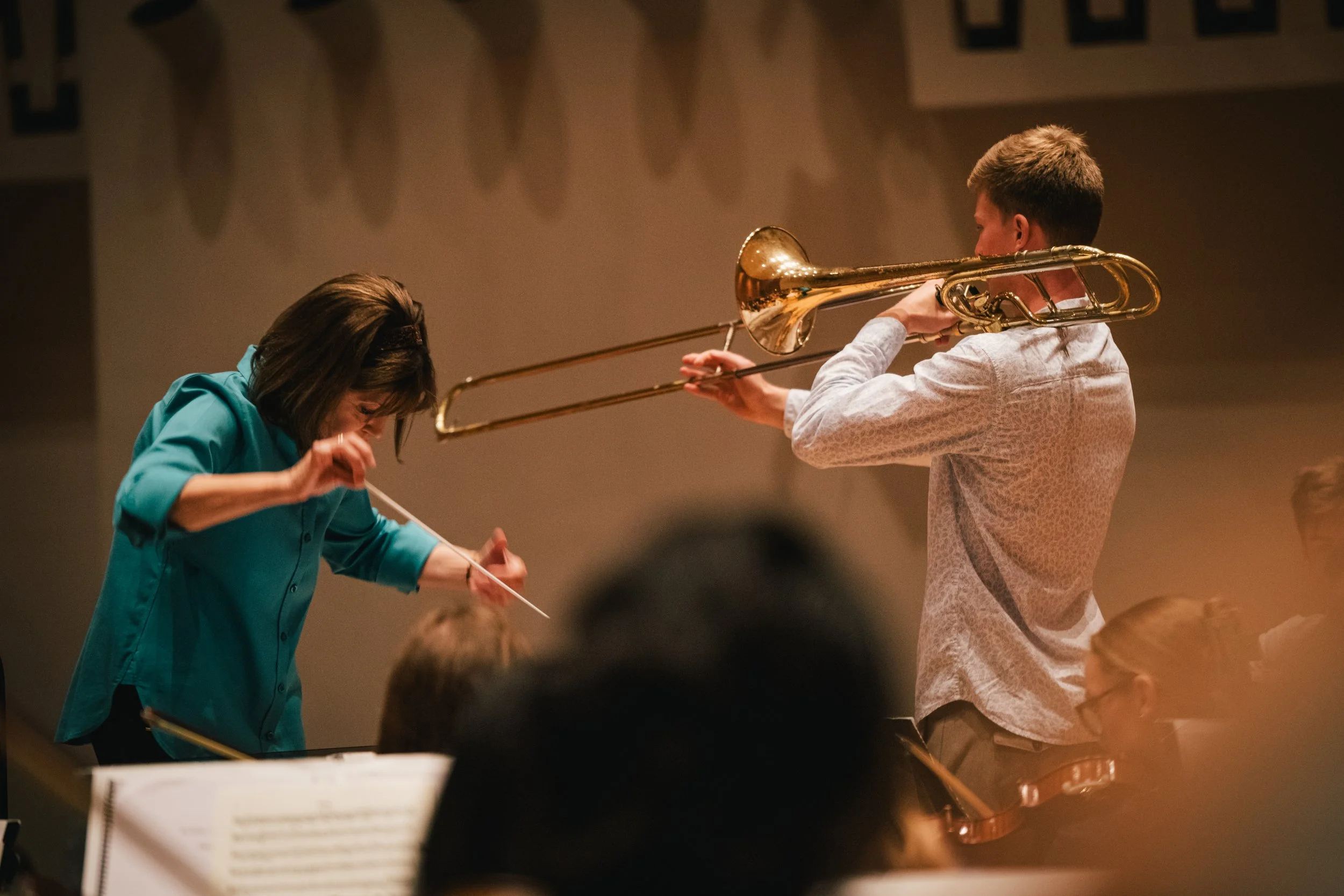 A woman conducting an orchestra with a baton and a man playing a trombone during a performance.