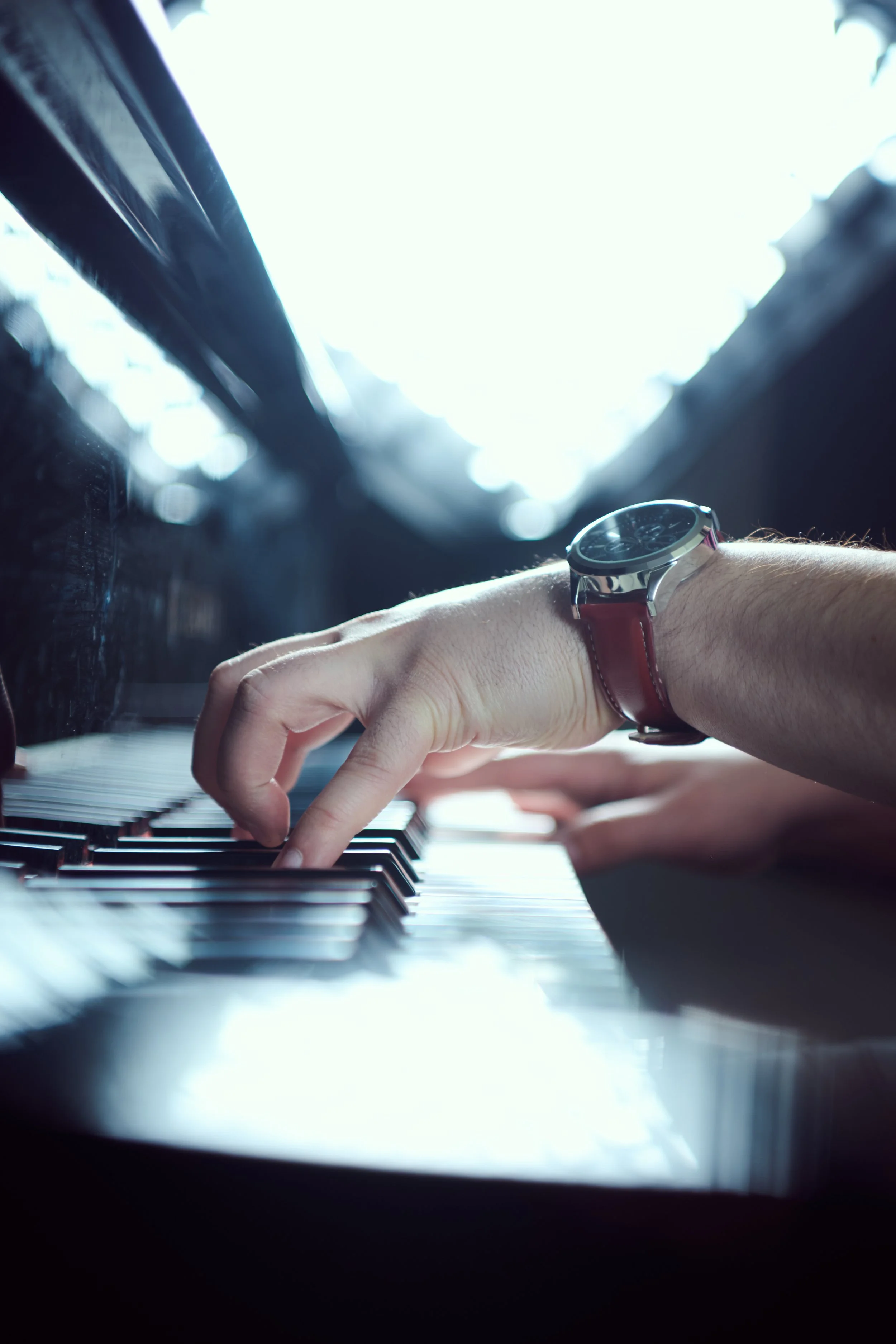 A person playing the piano, with their hand on the keys, wearing a watch with a leather strap.