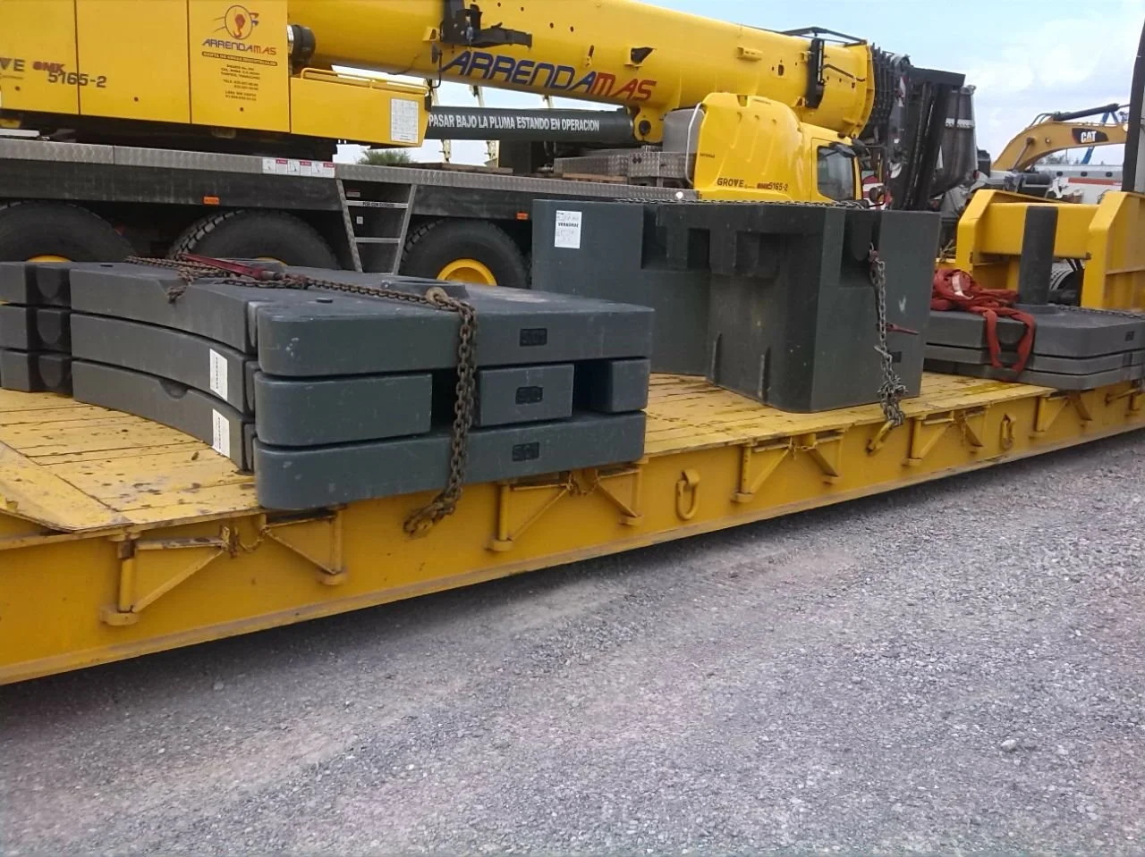 Plataforma de transporte con maquinaria pesada y partes de equipo de construcción en un entorno exterior.