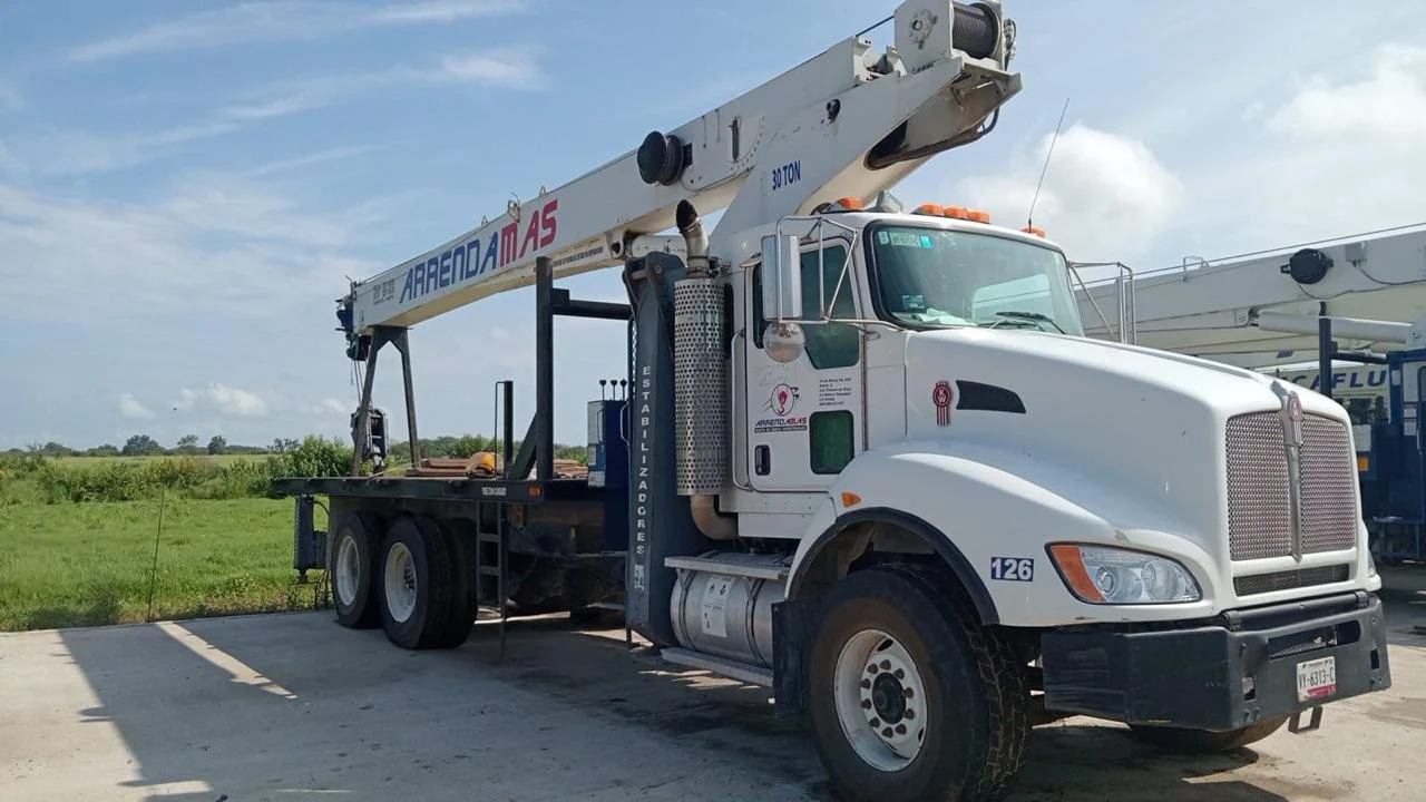 Camión grúa blanco con logotipo y texto en español en un área abierta