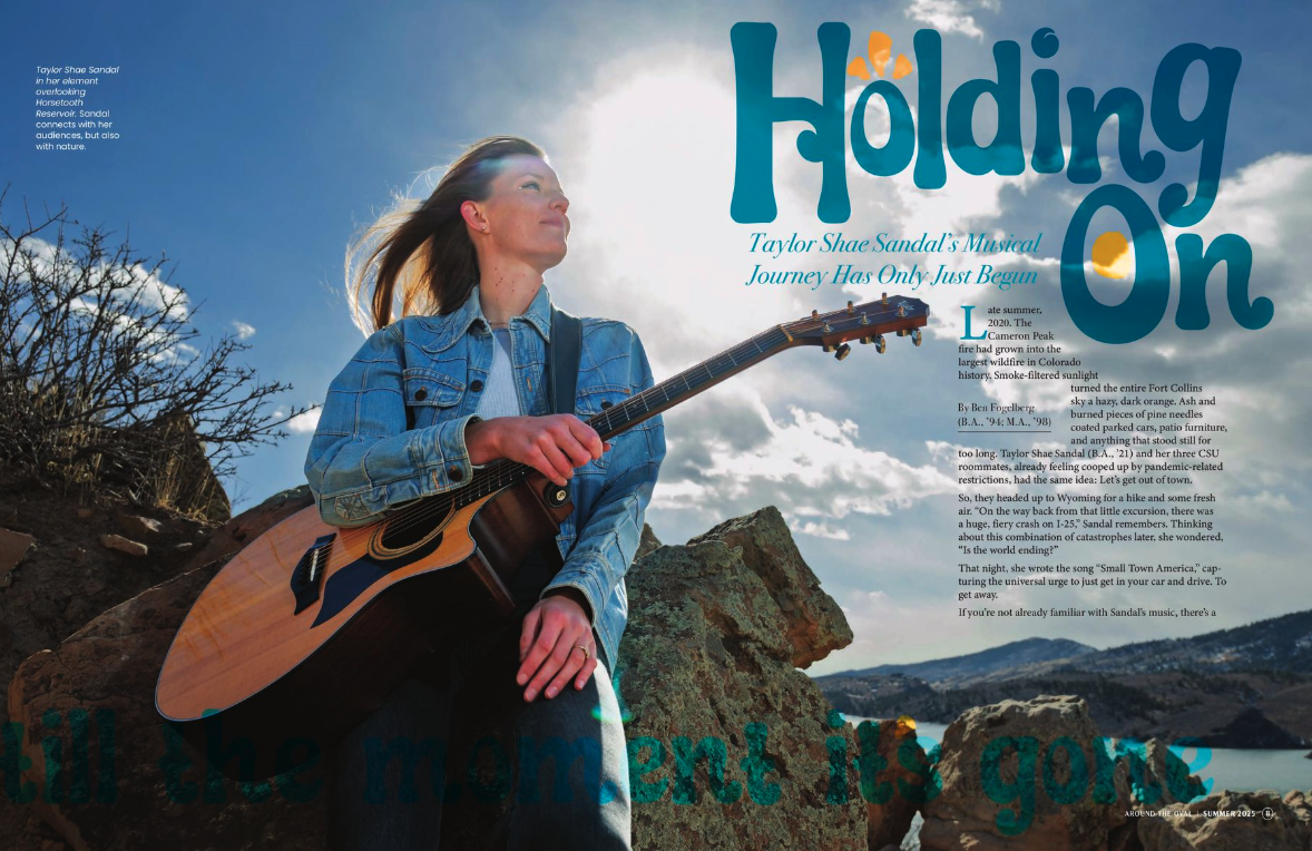 A young woman with long hair wearing a denim jacket holding an acoustic guitar, sitting on rocks outdoors with a scenic landscape, blue sky, and clouds in the background.