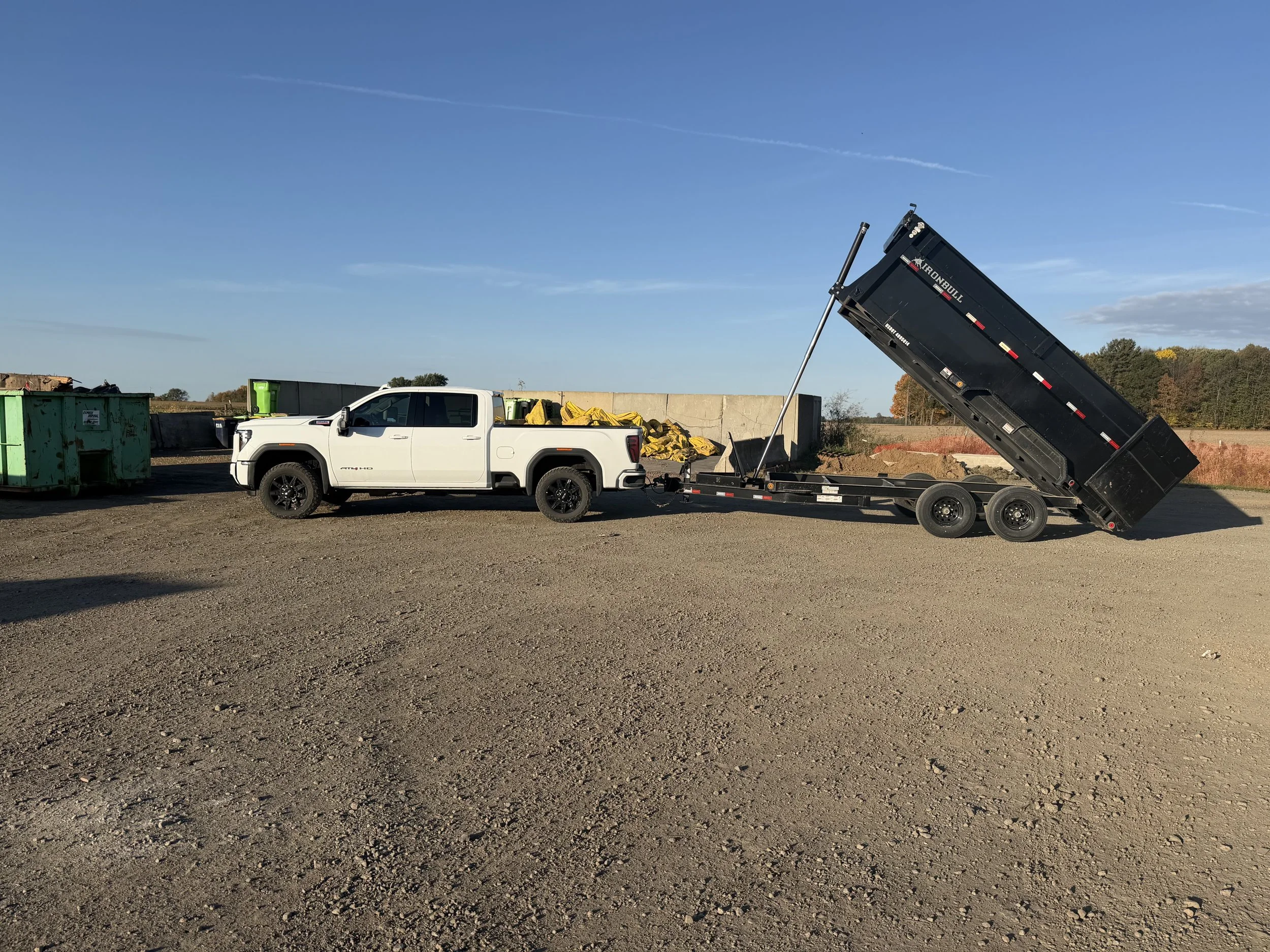 White pickup truck towing an HPC Contracting trailer with its bed raised.