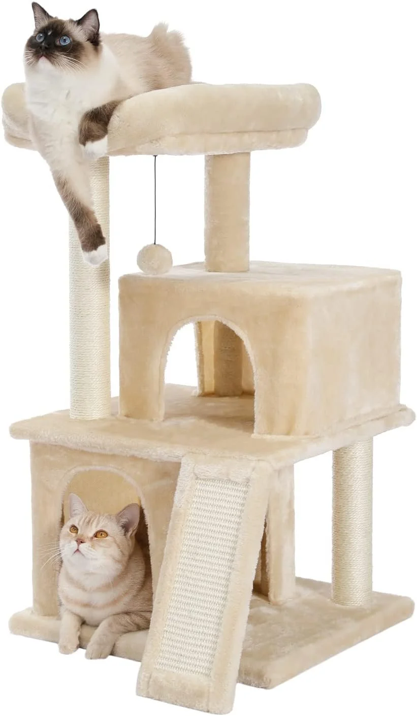 A beige multi-level cat tree with a scratching post, a ramp, and a hanging toy, with a Siamese cat lounging on the top platform and a British Shorthair sitting inside the lower cubbyhole.