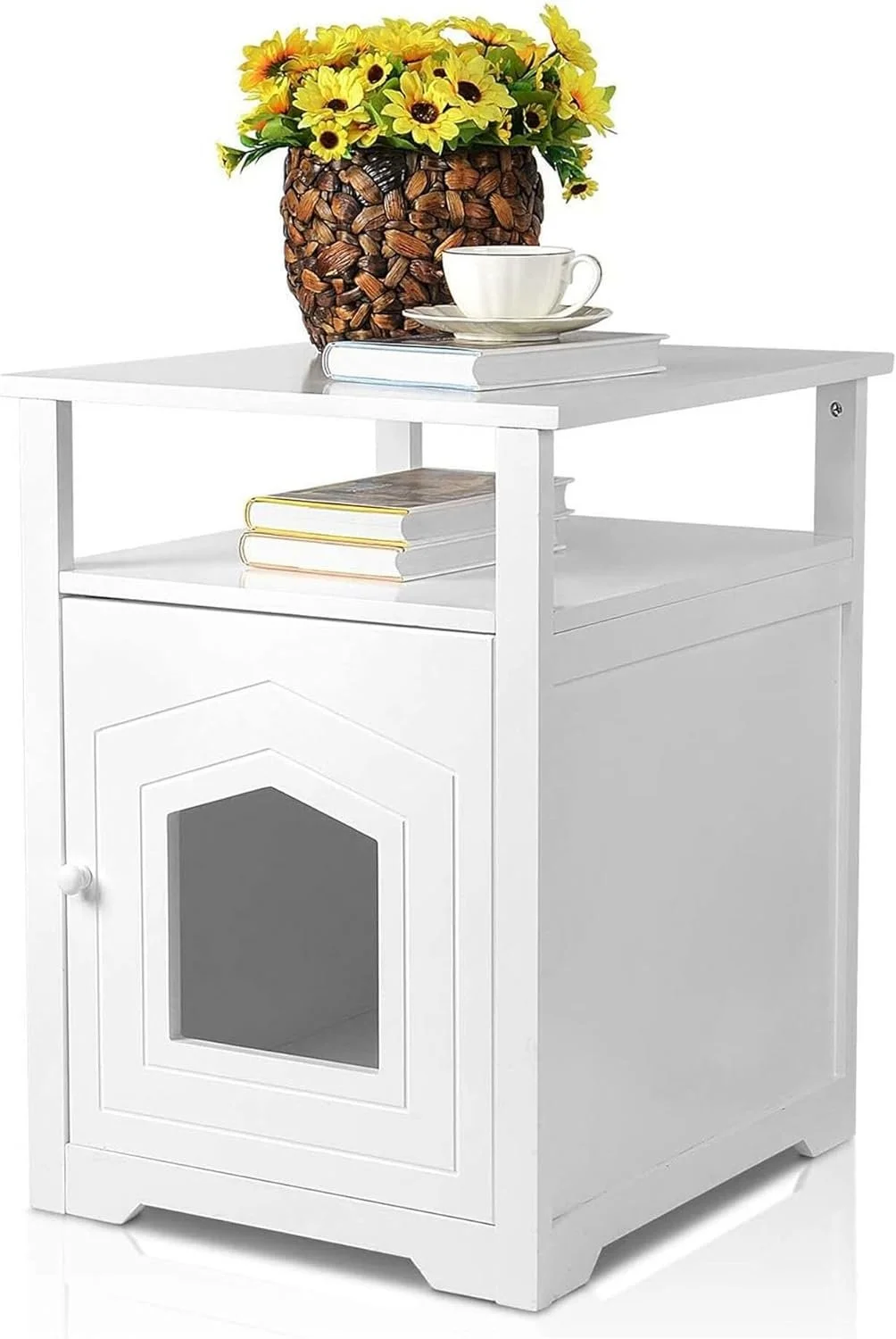 A white wooden side table with a glass window on the front door. On top, there is a stack of books, a white teacup with a saucer, and a large decorative vase filled with yellow sunflowers.