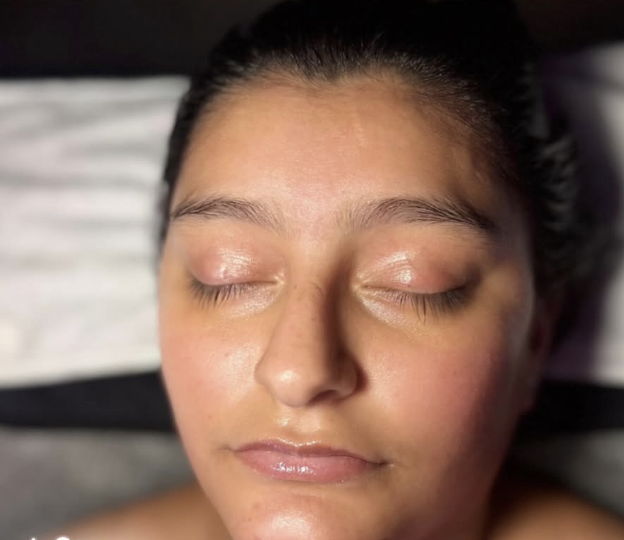 Close-up of a woman with closed eyes, smooth skin, and shiny lips, resting with head on a pillow.