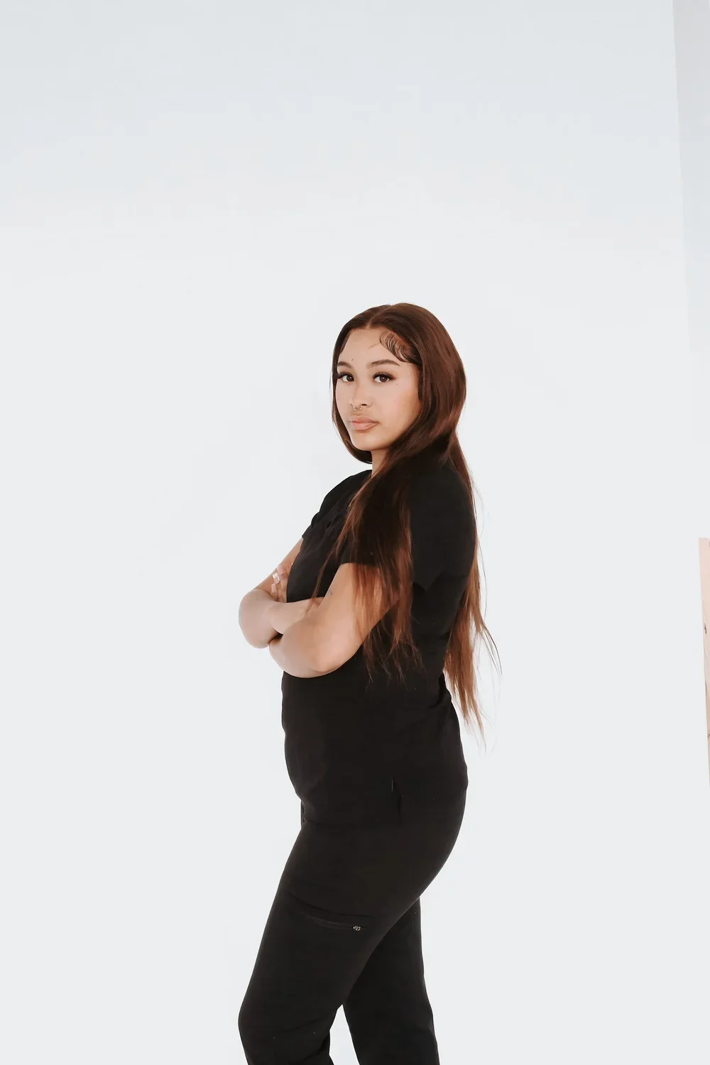 A woman with long brown hair standing with arms crossed against a plain white background.