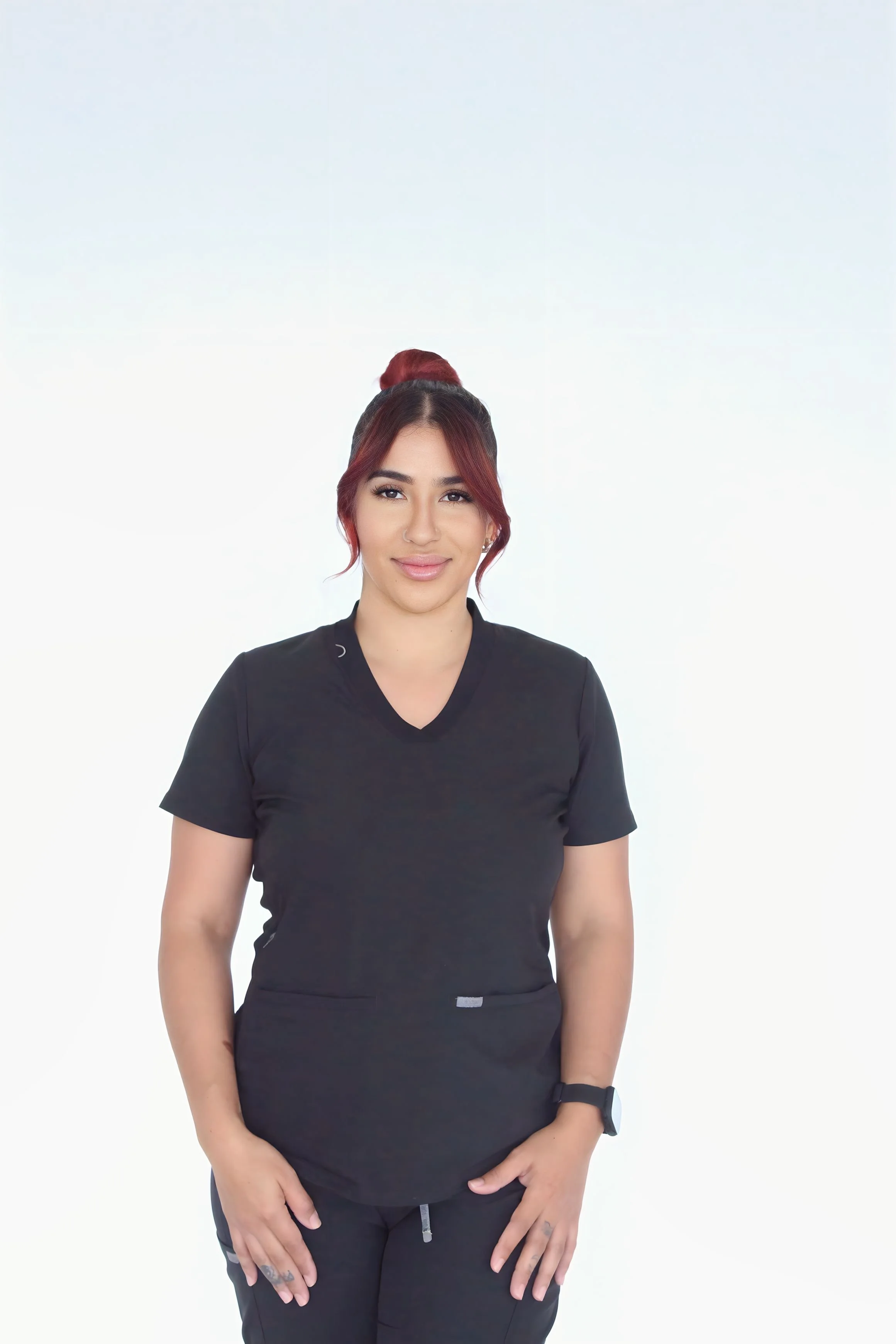 A woman in black scrubs standing with arms crossed, smiling in front of a plain white wall.