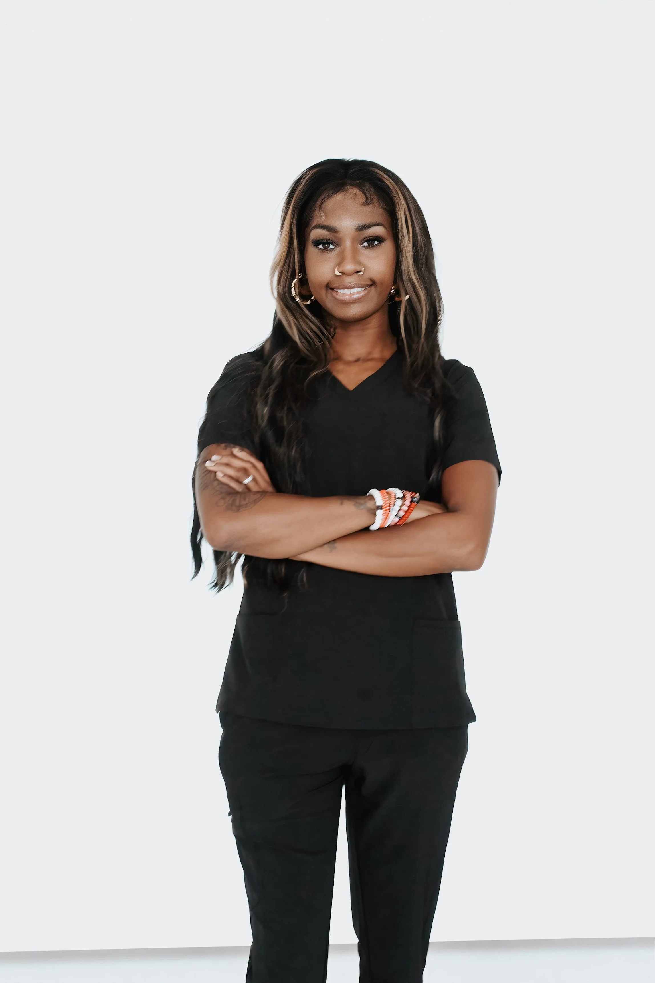 Young woman with long dark hair wearing black casual clothes, standing with arms crossed and smiling, against a plain white background.