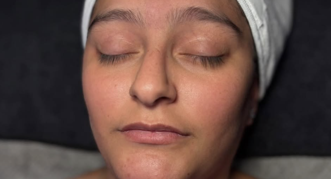 A woman with closed eyes relaxing during a facial treatment, lying on a treatment bed with a headband.