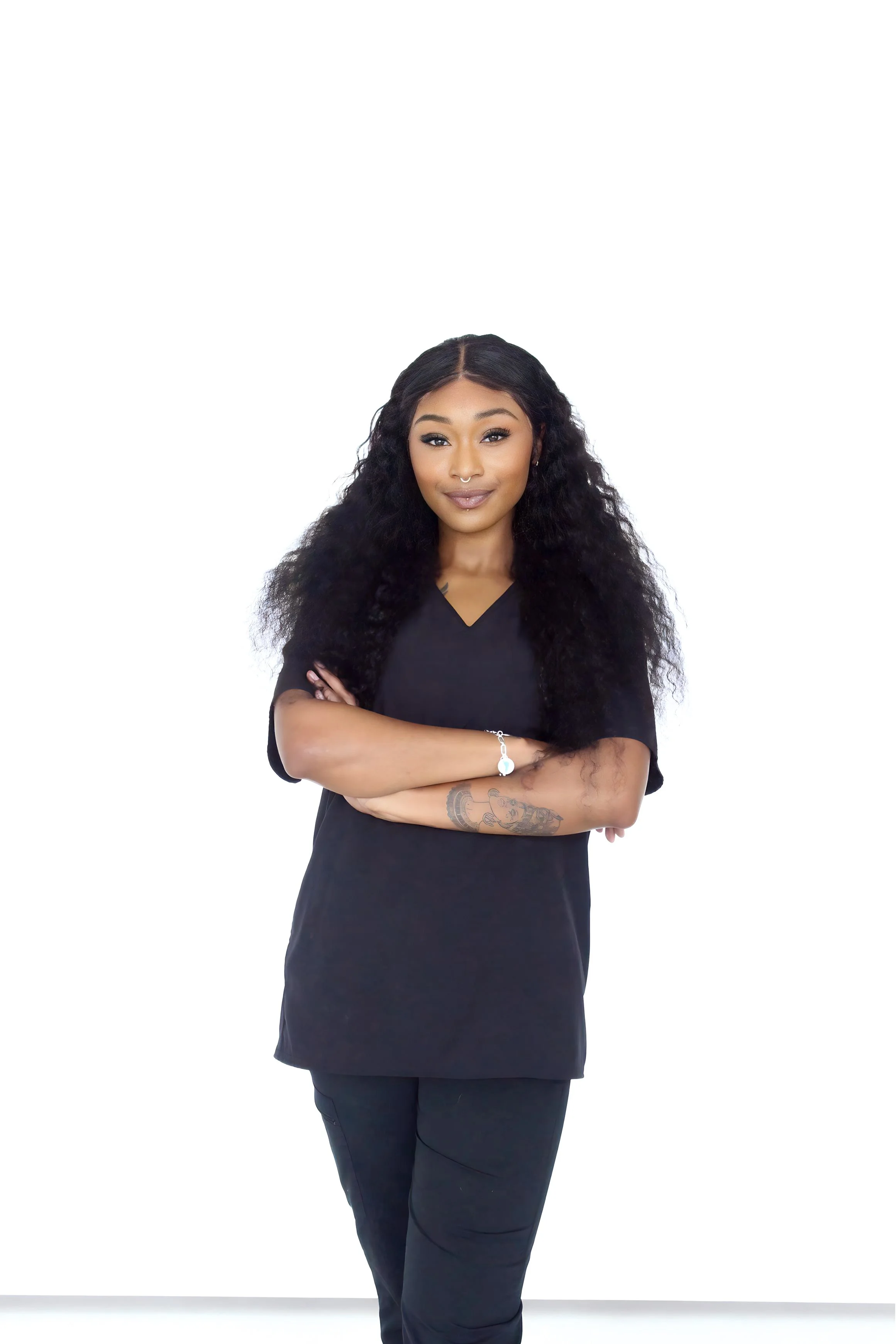 Young woman in black scrubs smiling, standing against a white background.
