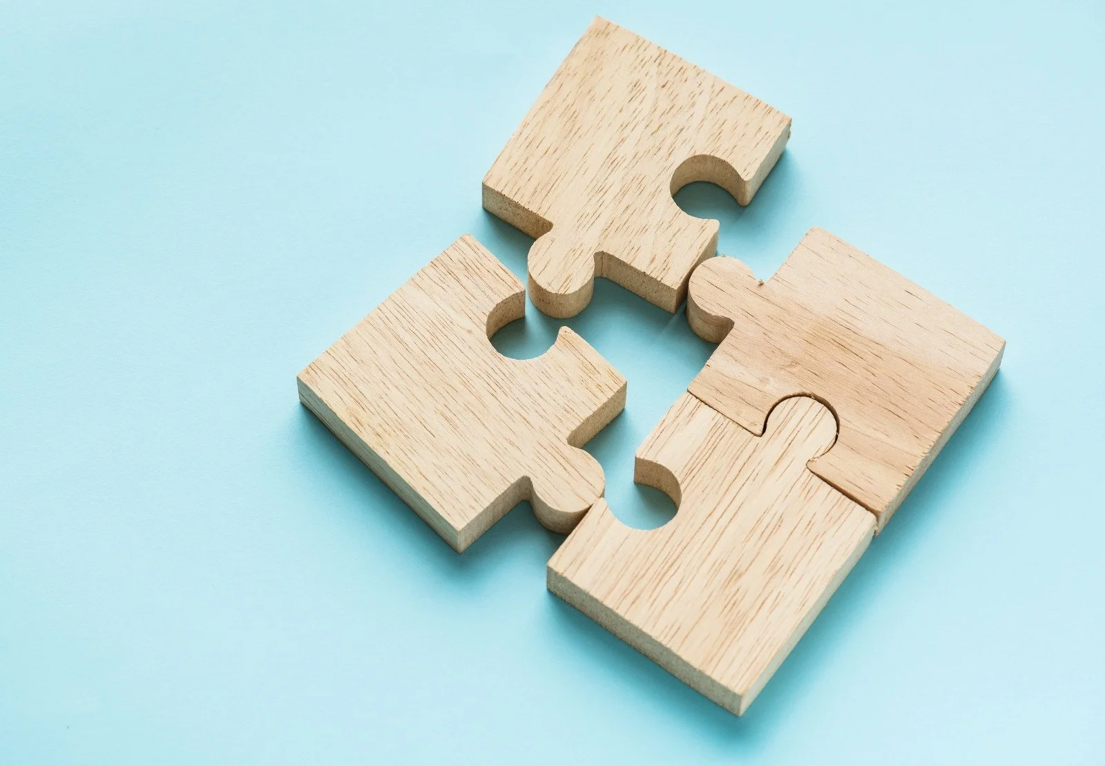 Four wooden puzzle pieces on a light blue background, fitting together for our story on about us