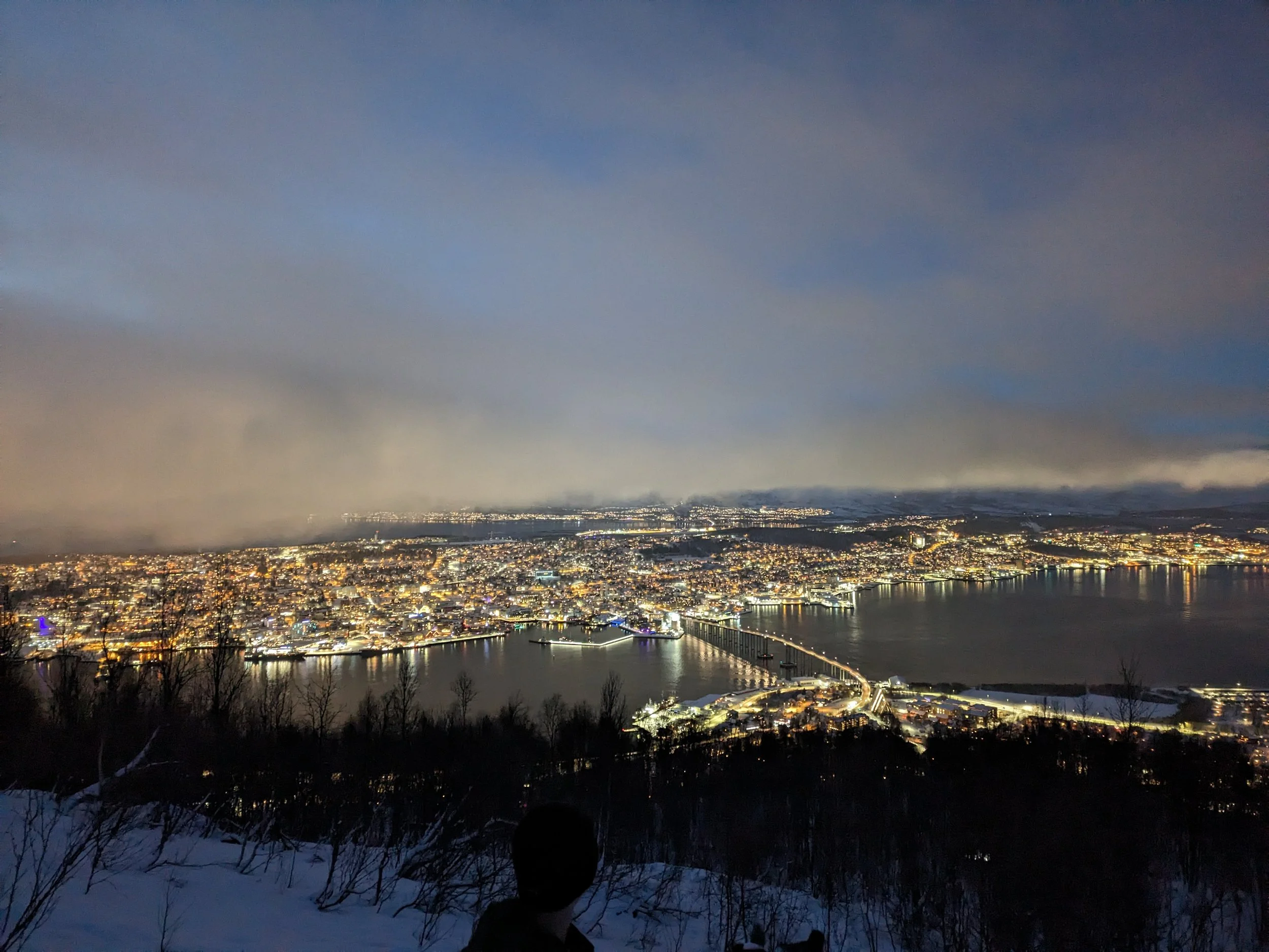 The city of Tromsø glowing under the Arctic night sky. A breathtaking view from above, showing the true scale of the city.