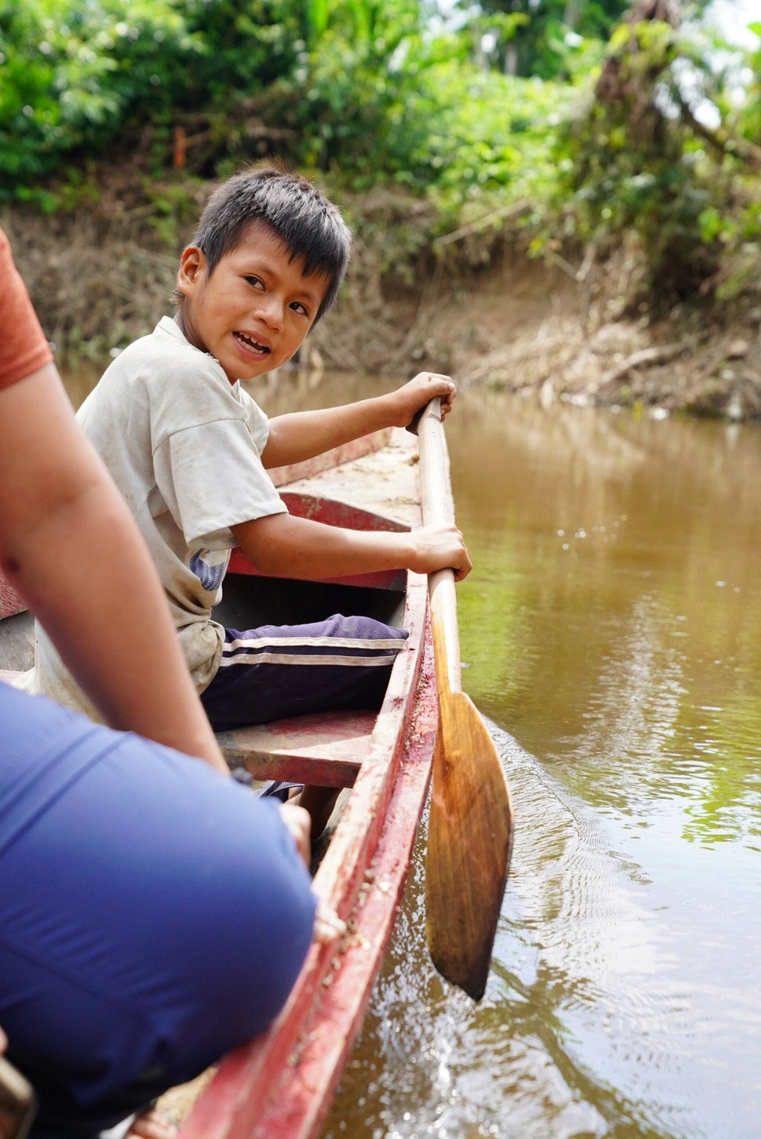 A young boy paddling a canoe on a river surrounded by trees.