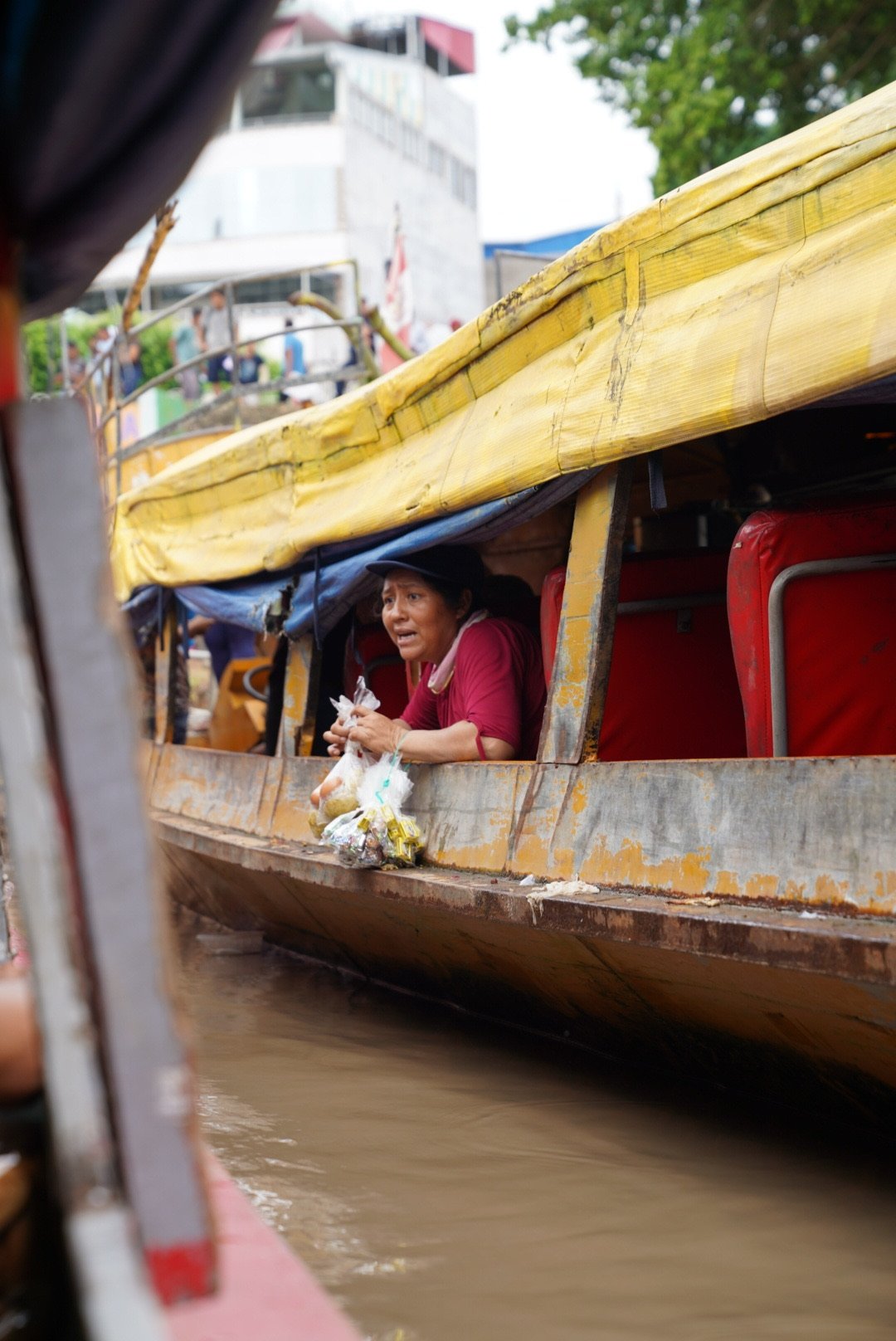 A woman on a boat holding a small bag, looking distressed, with a busy urban area in the background.