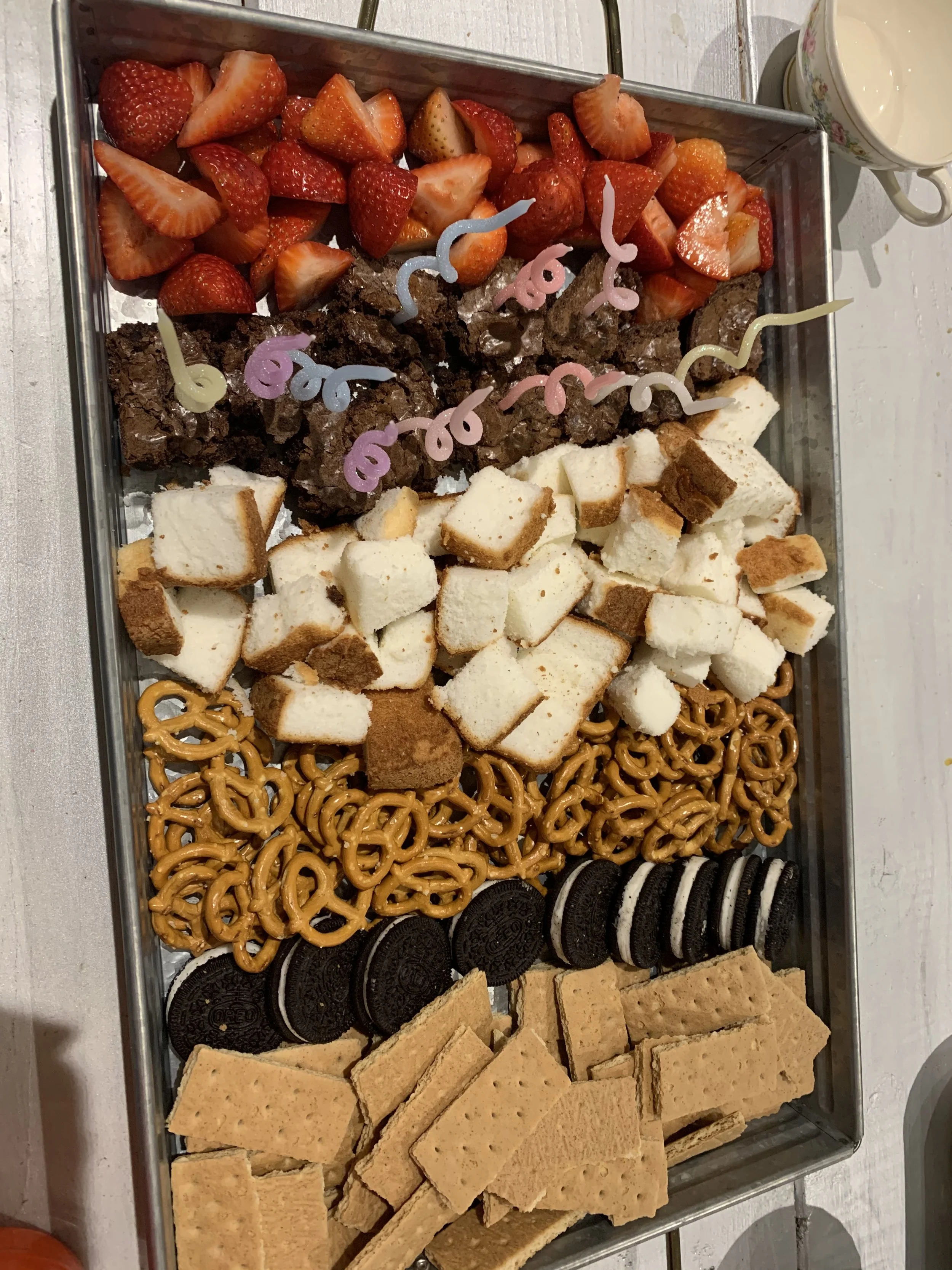 A tray filled with strawberries, brownies, vanilla cookies, pretzels, Oreo cookies, and saltines.