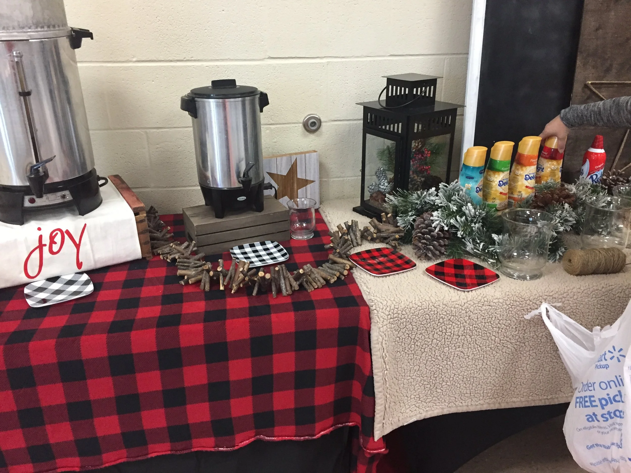 Table with a red and black checkered tablecloth displaying holiday-themed decorations, snack containers, and a small glass container near a white and black checkered plate.