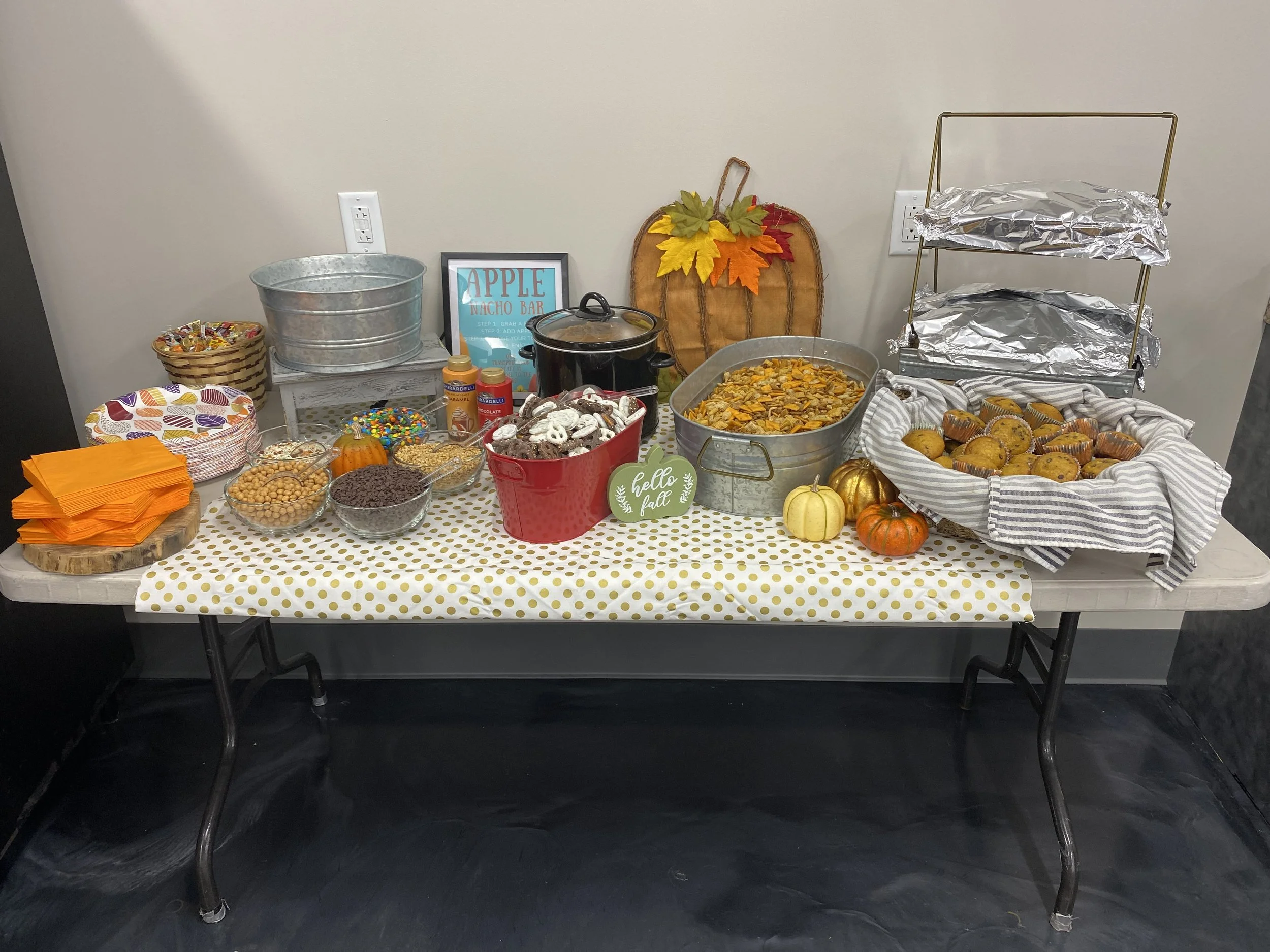 A fall-themed snack table with various candies, baked goods, and decorations on a polka dot tablecloth, featuring a 