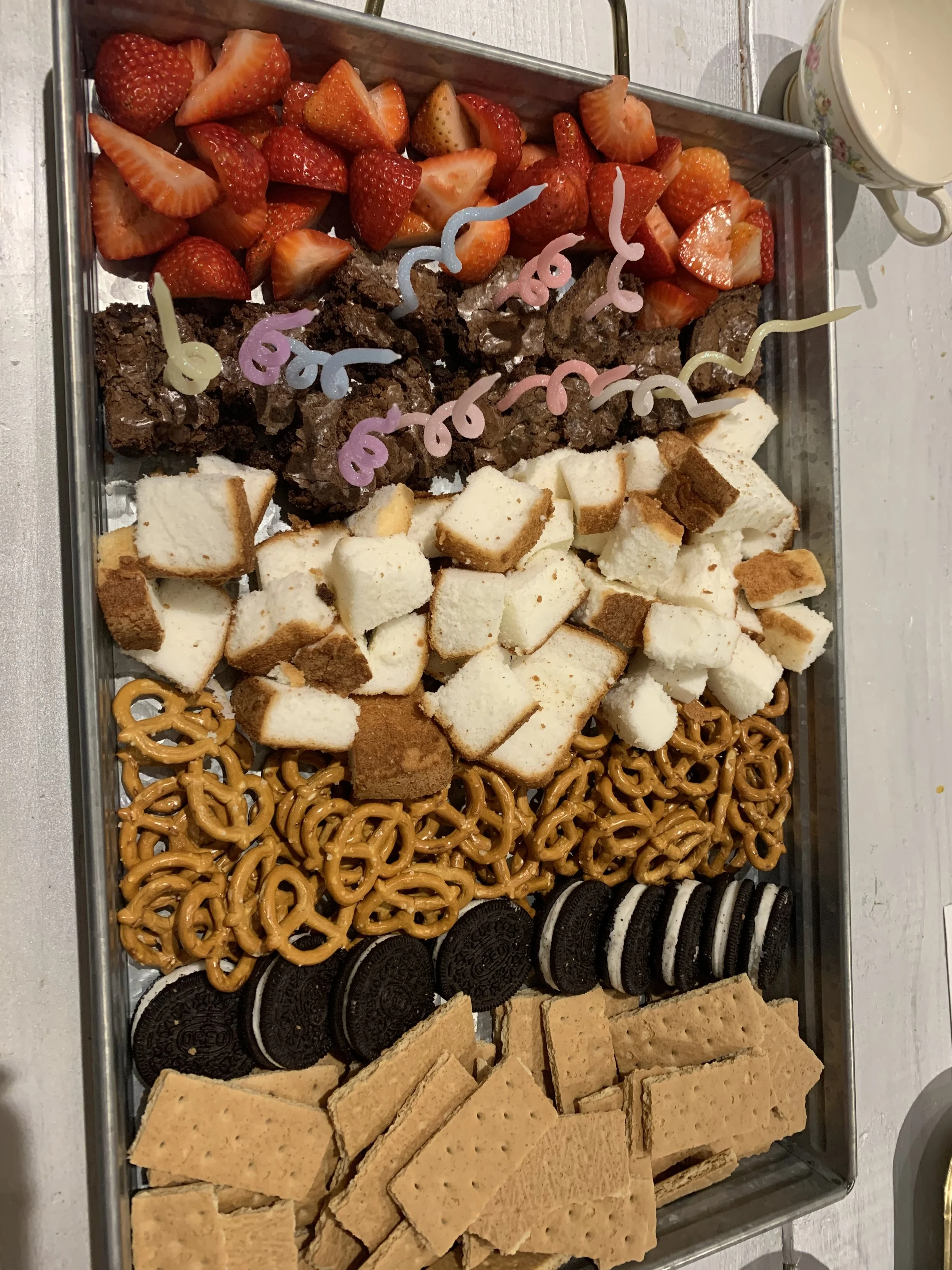 A tray filled with various sweet treats, including strawberries, brownies with colorful squiggly decorations, cut-up pound cake, pretzels, Oreo cookies, and broken pieces of vanilla-flavored fudge.