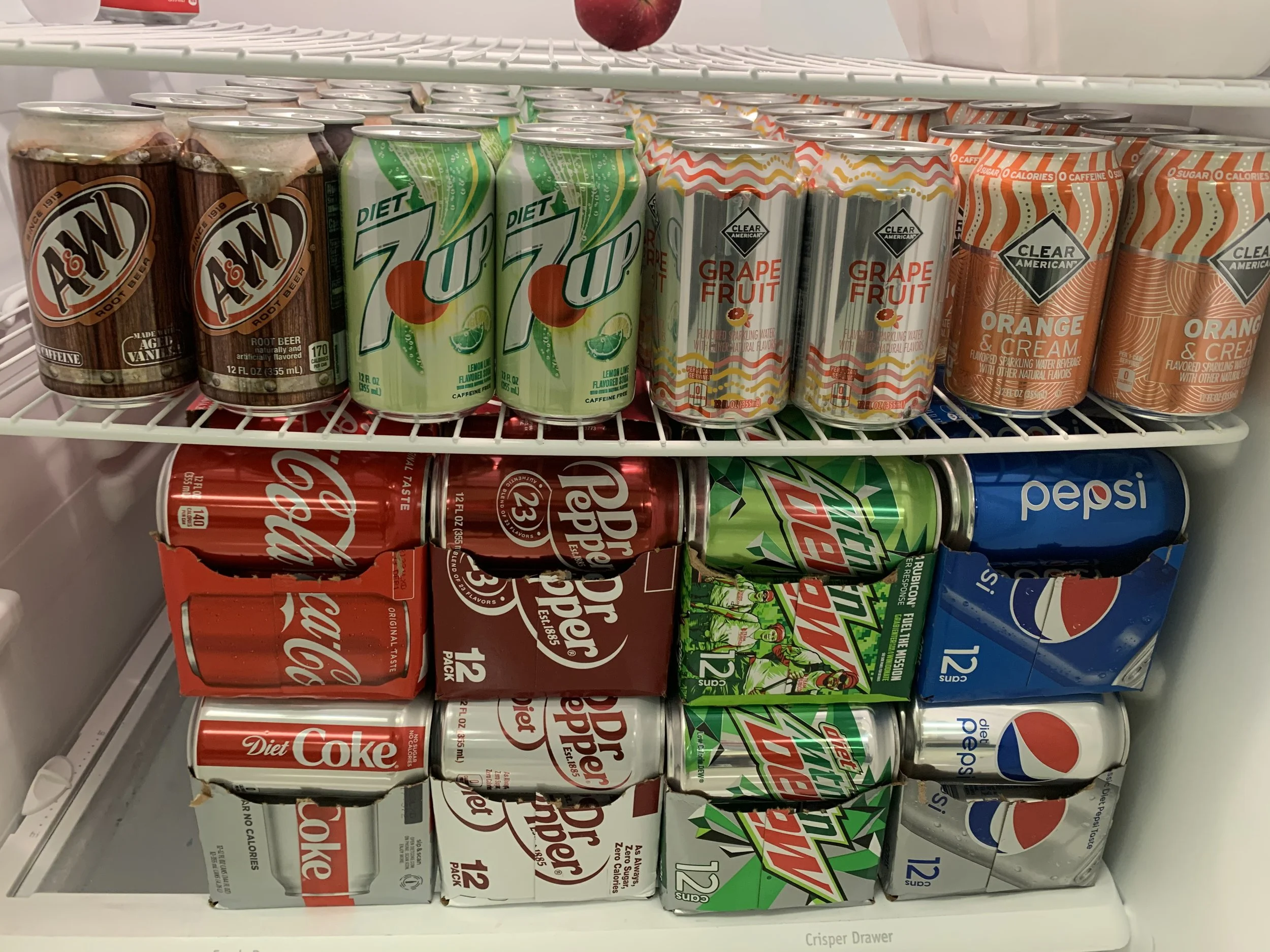 A freezer shelf stocked with various cans of soda, including Diet 7UP, Clear American Grape Fruit, Clear American Orange & Cream, Coca-Cola Diet, Dr. Pepper, Mountain Dew, and Pepsi.