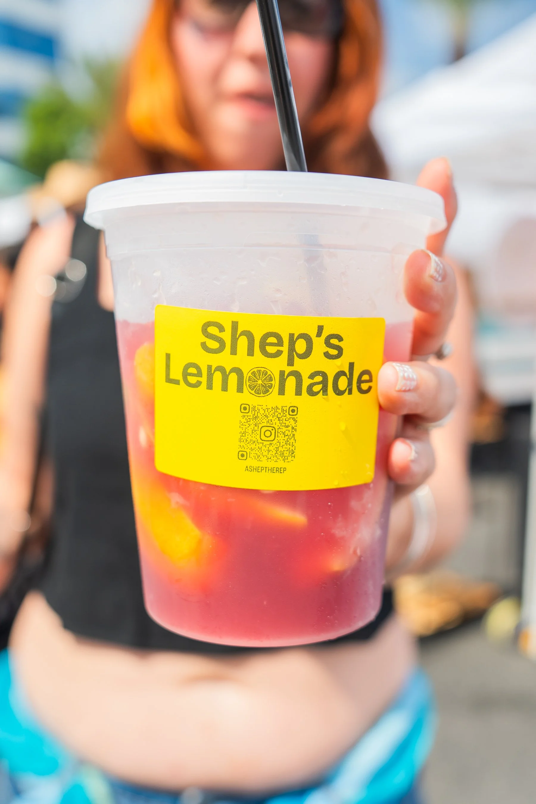 A guest holding a pink Shep’s Lemonade with fresh citrus and a bright yellow branded label.