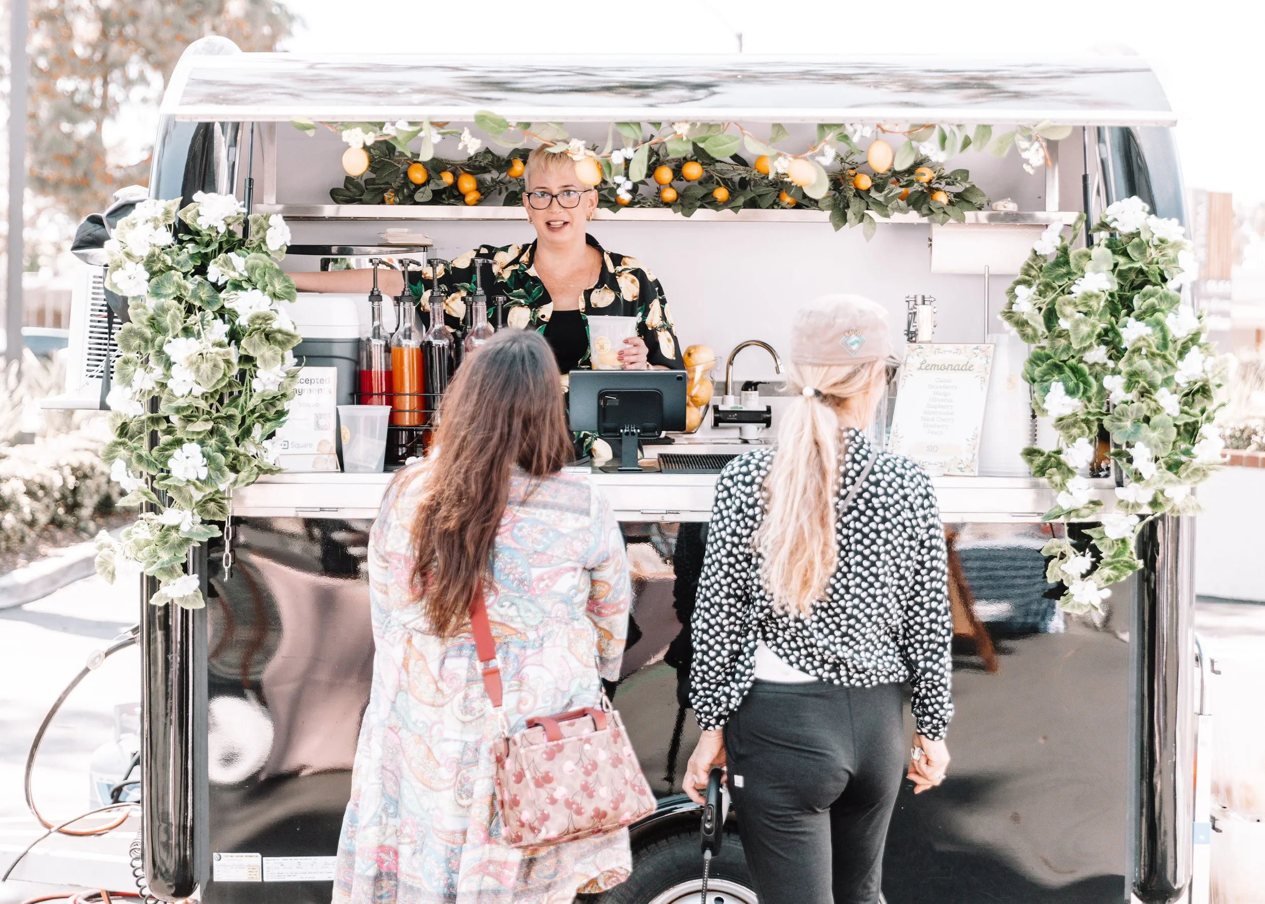 Shep welcoming guests at the fresh lemonade trailer, decorated with citrus, greenery, and white flowers.