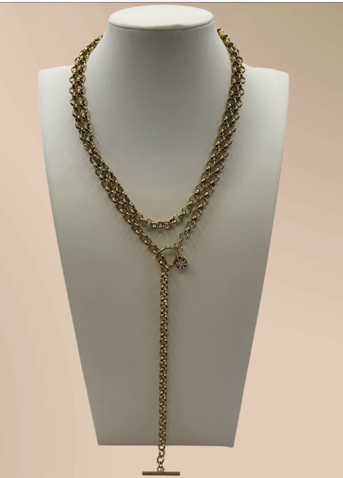 Gold layered chain necklace with a decorative ring and small charm, displayed on a white jewelry bust.