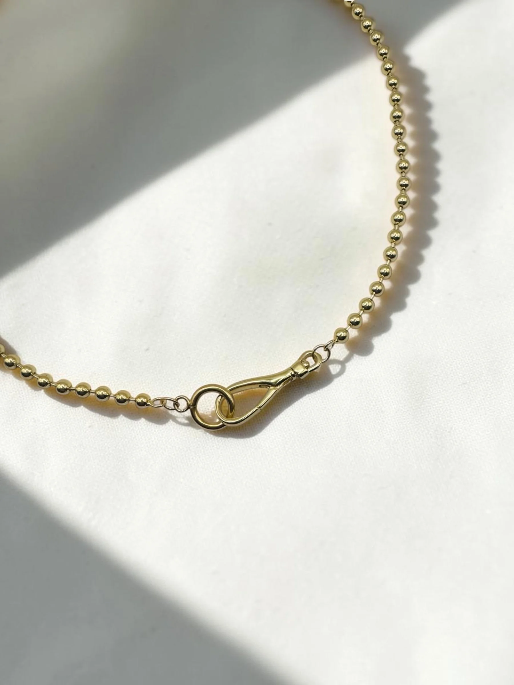 Close-up of a gold beaded necklace with a clasp, against a light blue background, with text reading 'CHAIN RULE Foundation'.