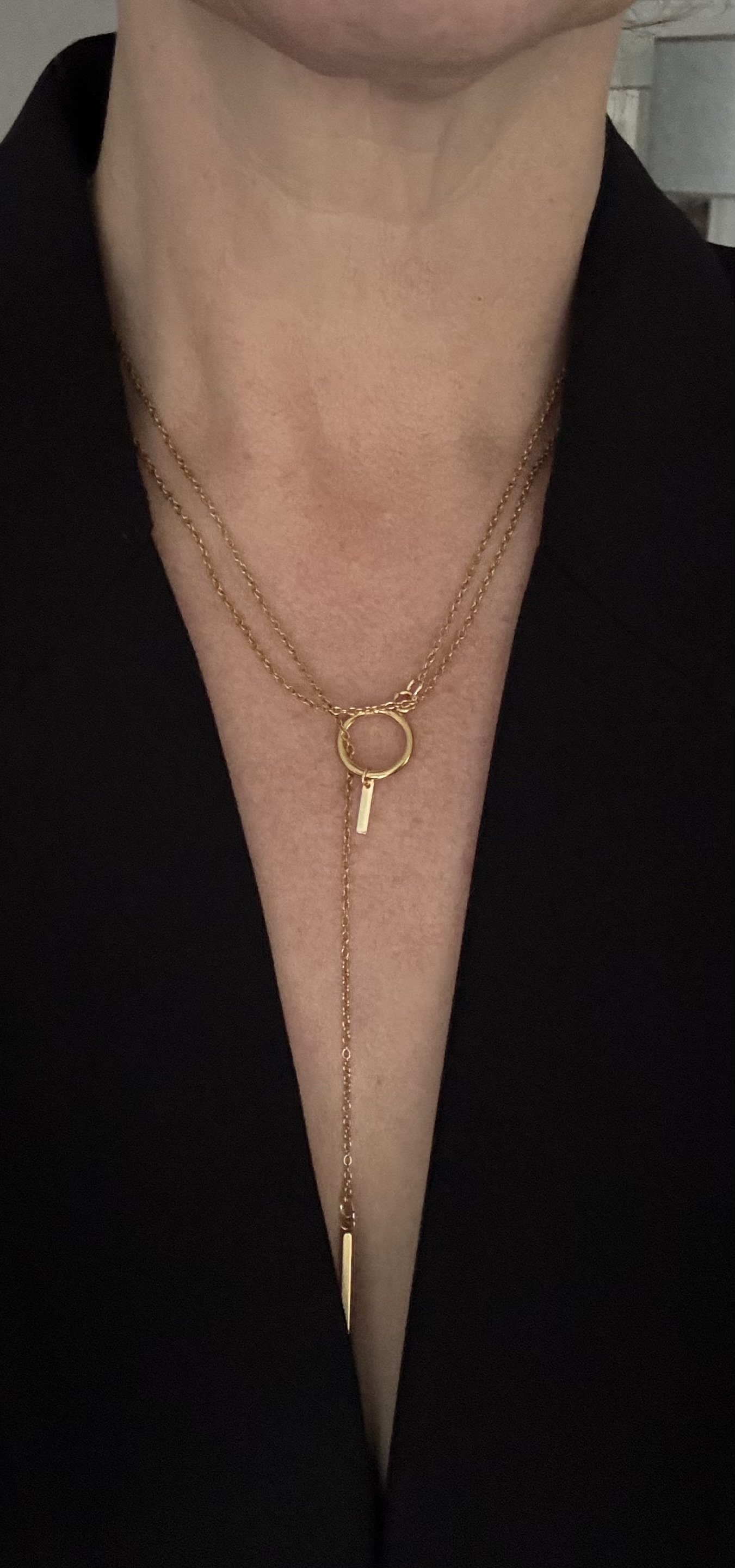 A close-up of a person's neck and chest showing Chain Rule Jewellery's PM/Luna layered gold necklace with circular and bar pendants, against a black clothing background.