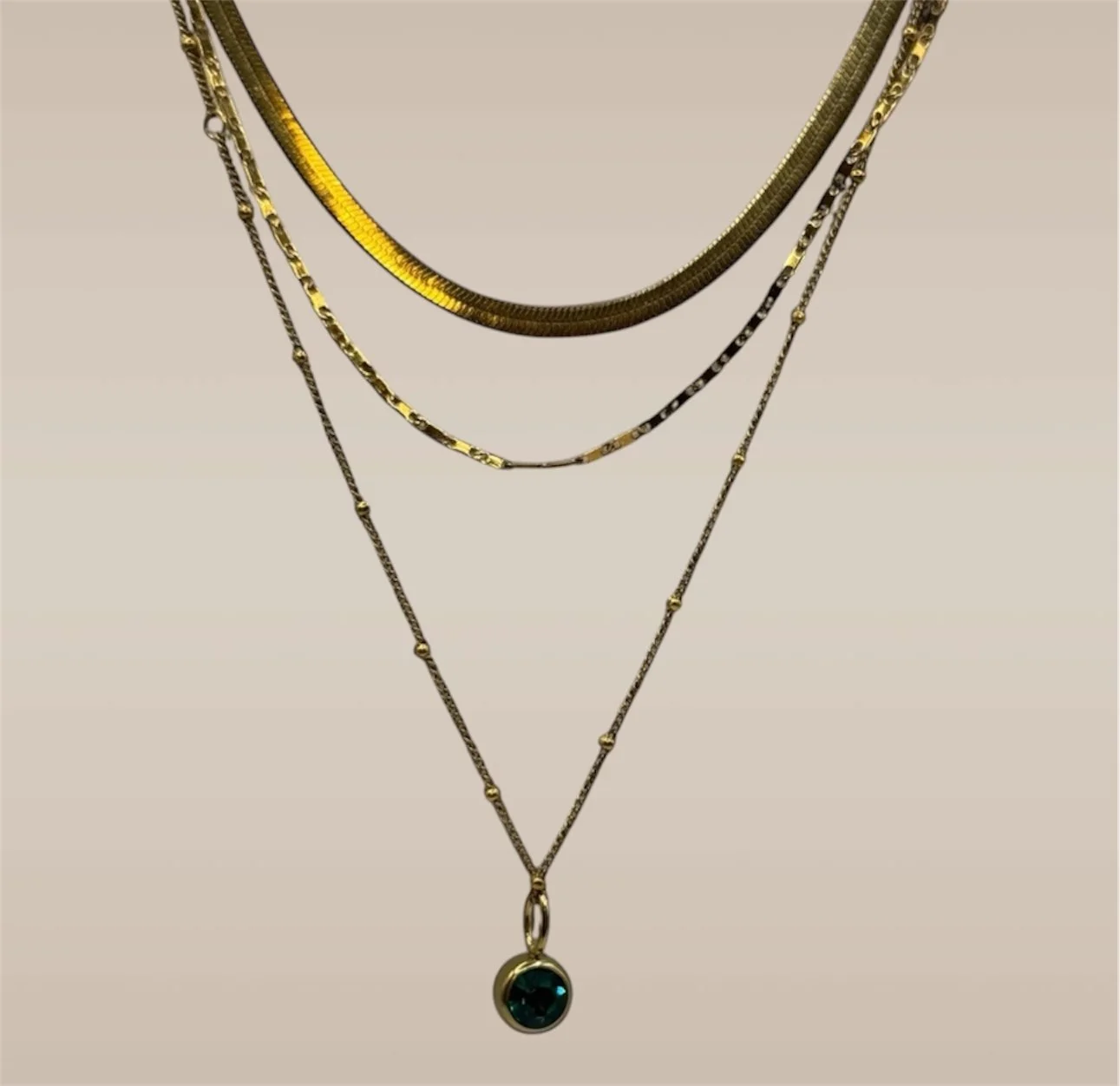 Multiple layered gold necklaces with one featuring a green gemstone pendant.
