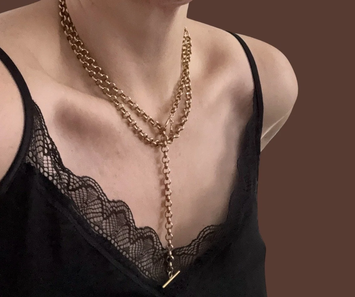 Close-up of a woman's neck and chest wearing layered gold chain necklaces and a black lace camisole.