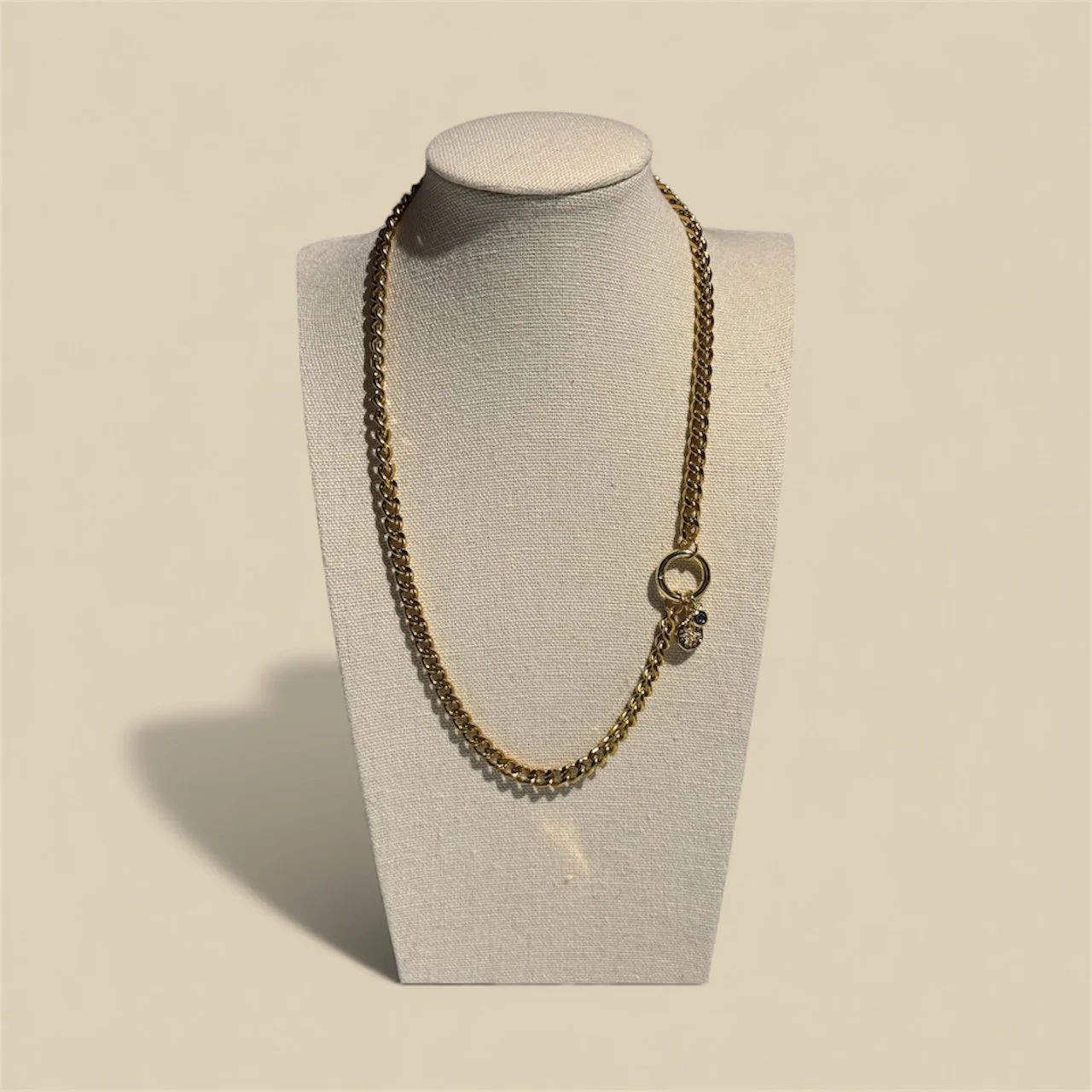 Gold chain necklace with charms displayed on a white jewellery bust