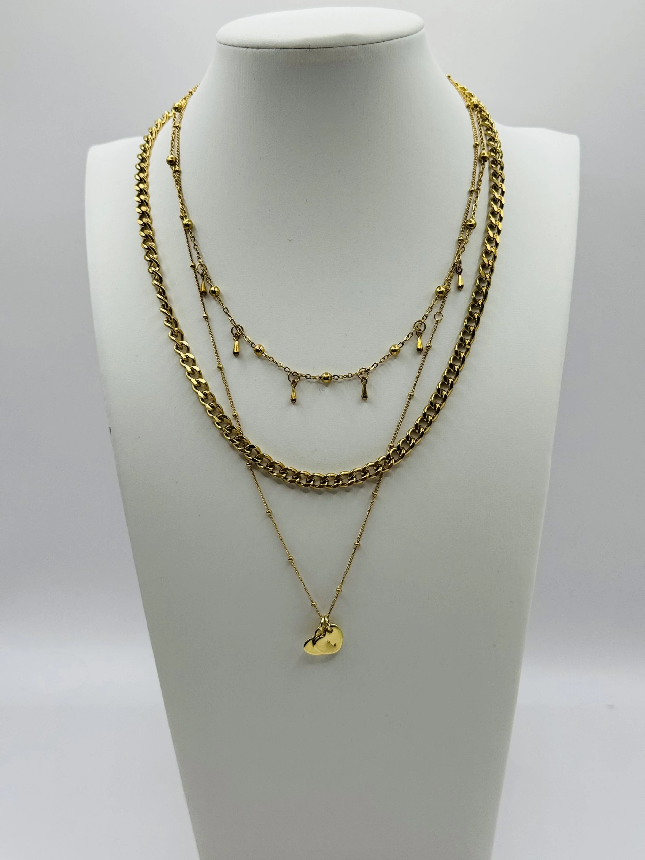 Three layered gold necklaces displayed on a white bust, varying chain styles and a diamond shaped pendant. Chain Rule Jewellery's layered stack includes the Dewdrop choker, snake chain and a dainty diamond shaped pendant