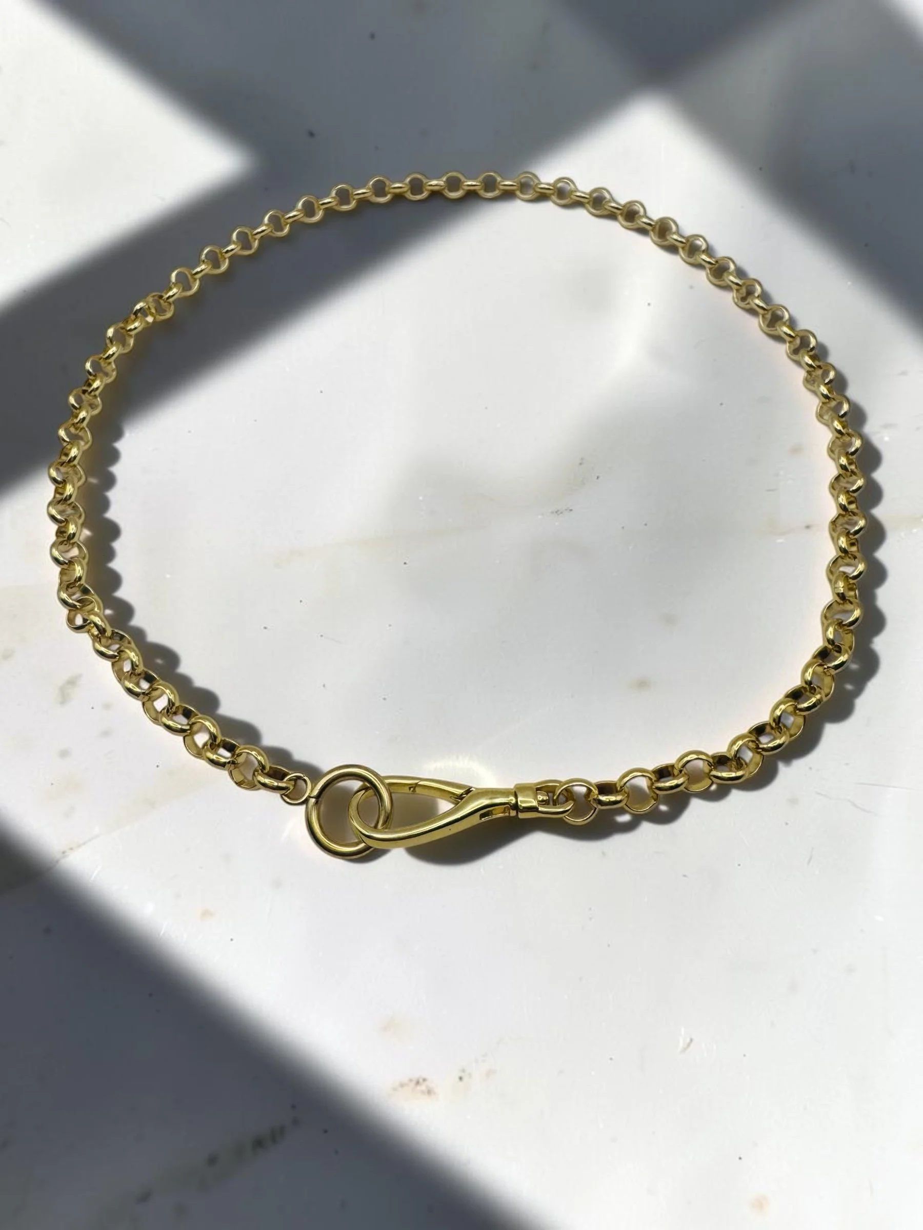 Close-up of a woman's neck and shoulder, showing gold jewelry including a chain necklace and bracelets. She is wearing a black top.