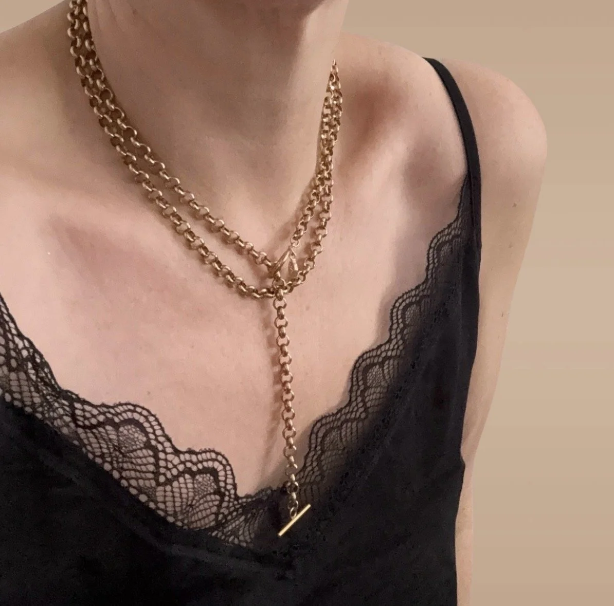 A person wearing layered gold chains around their neck, dressed in a black lace-camisk top with a scalloped lace trim.