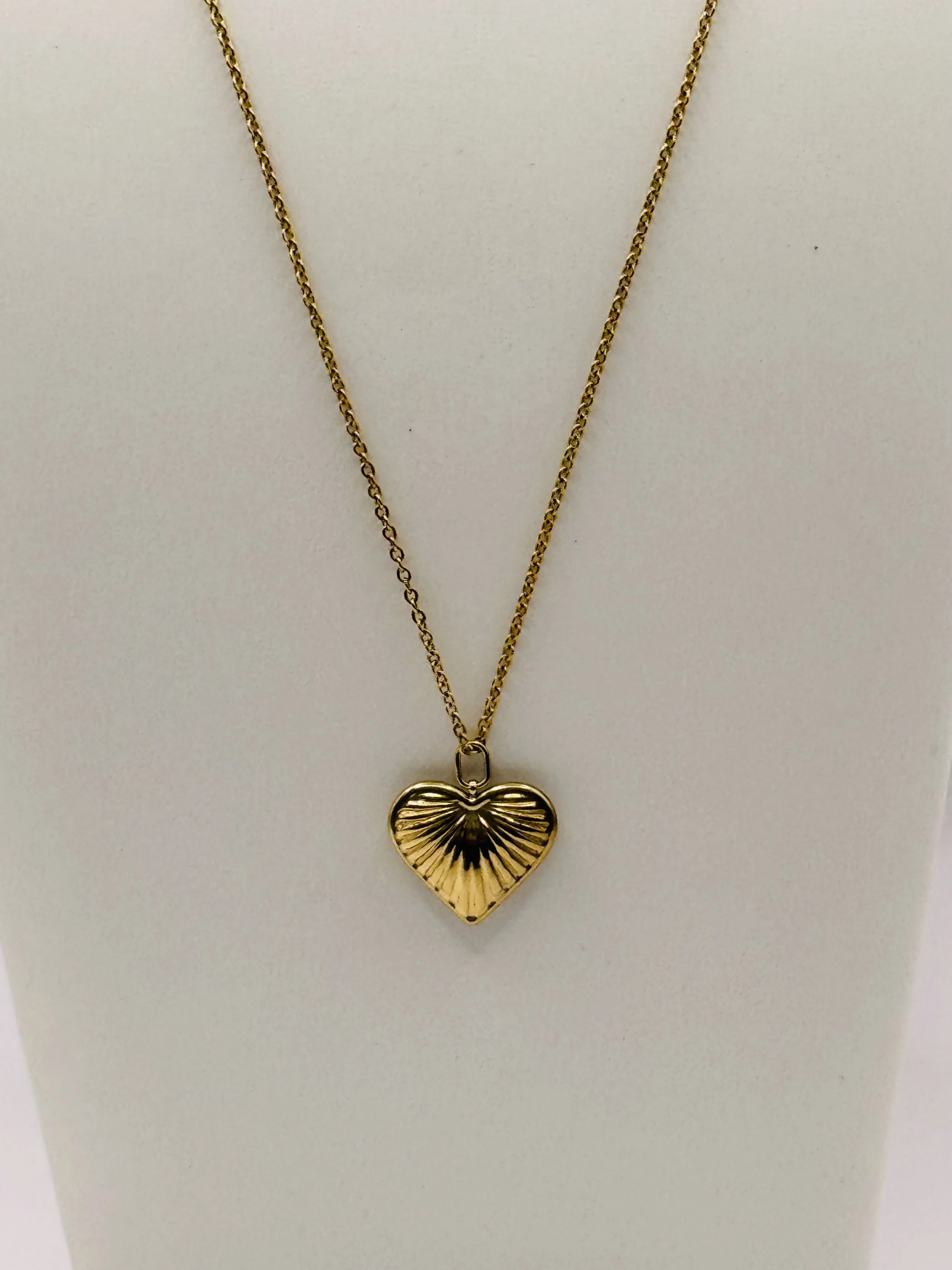 Gold heart-shaped pendant necklace with radiating lines, hanging on a gold chain against a white background.